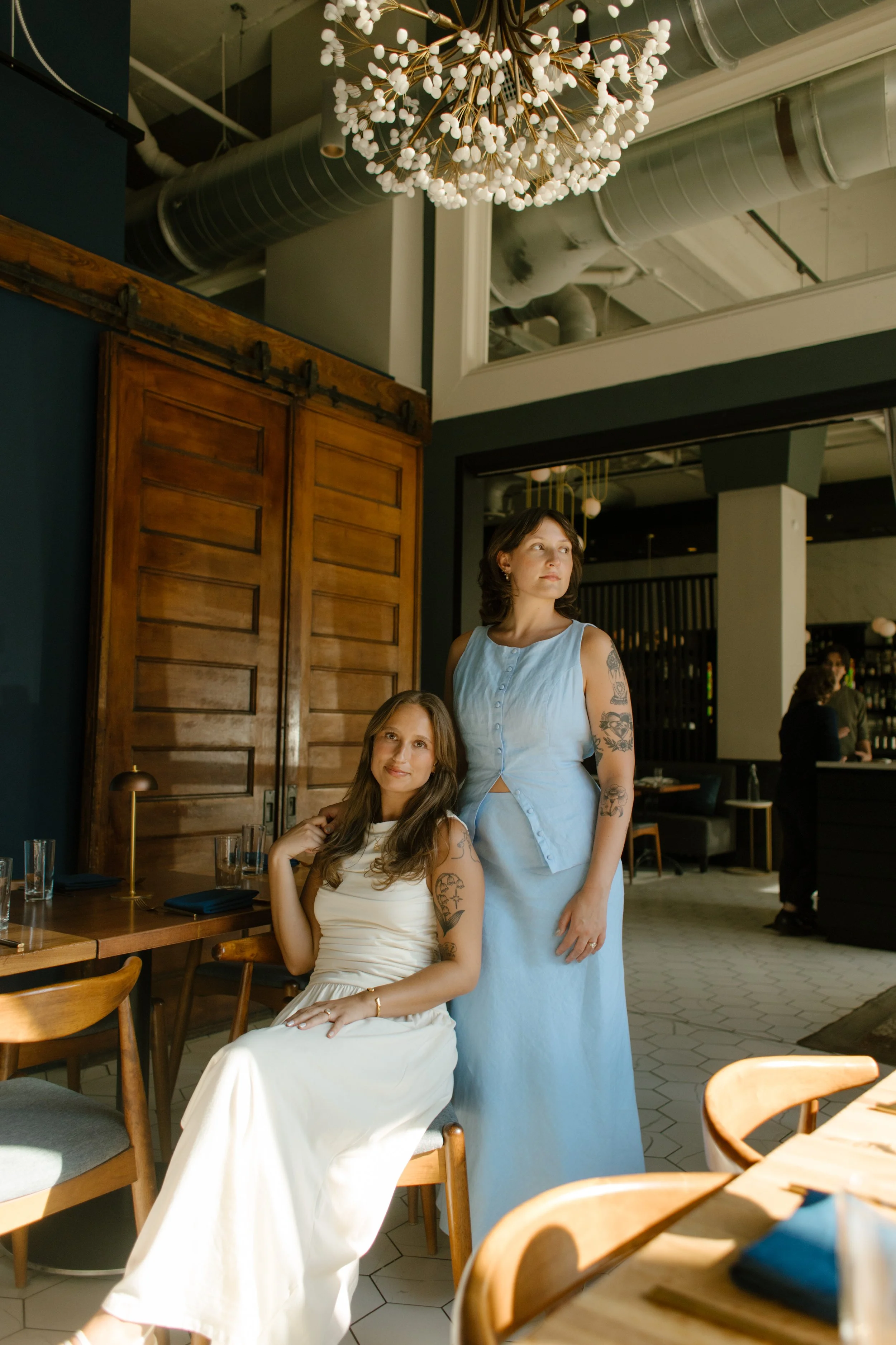 Editorial-style portrait of two brides inside a modern restaurant with warm natural light, photographed by a documentary wedding photographer.