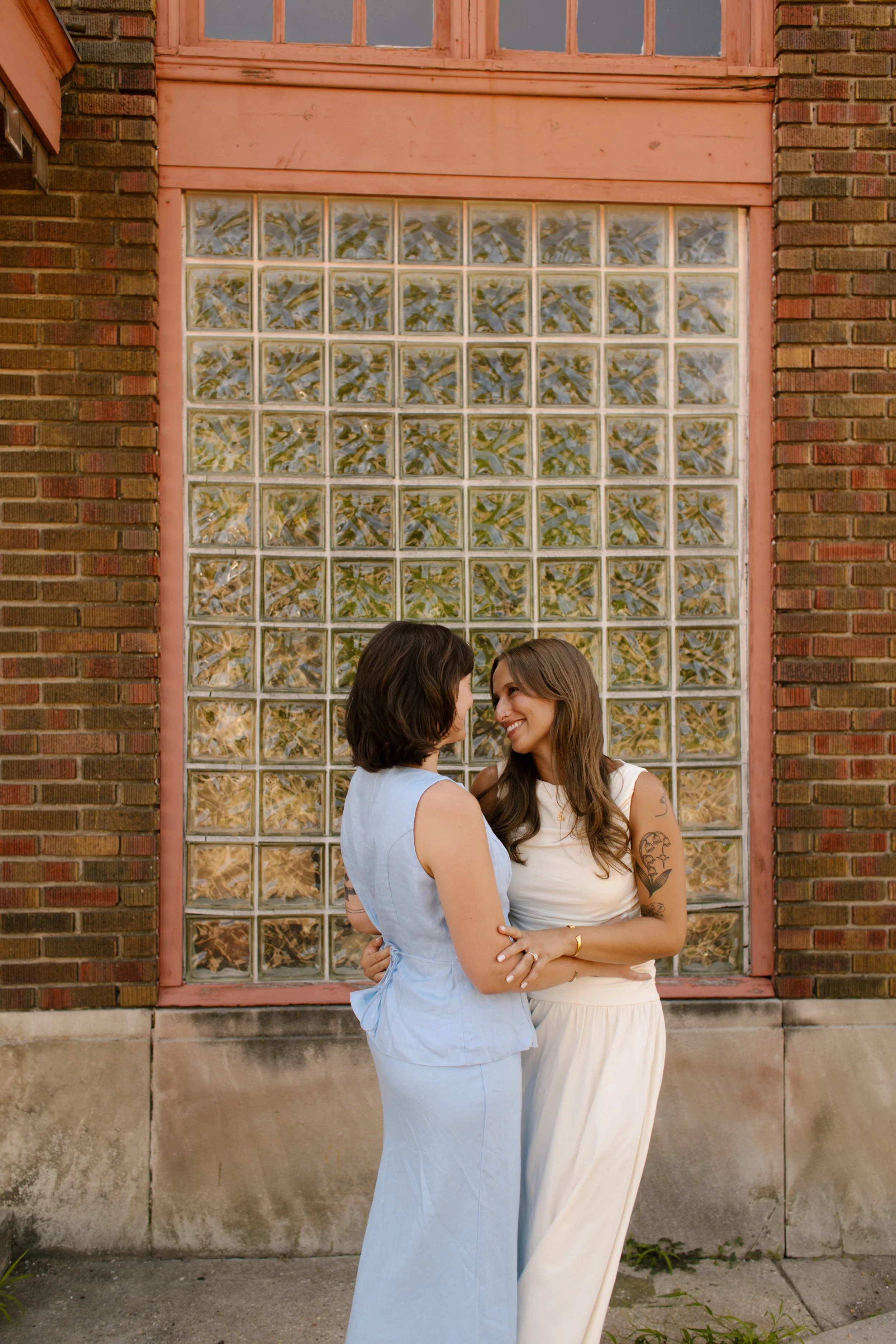 Couple embraces in front of a glass block wall during relaxed wedding portraits by a documentary wedding photographer.
