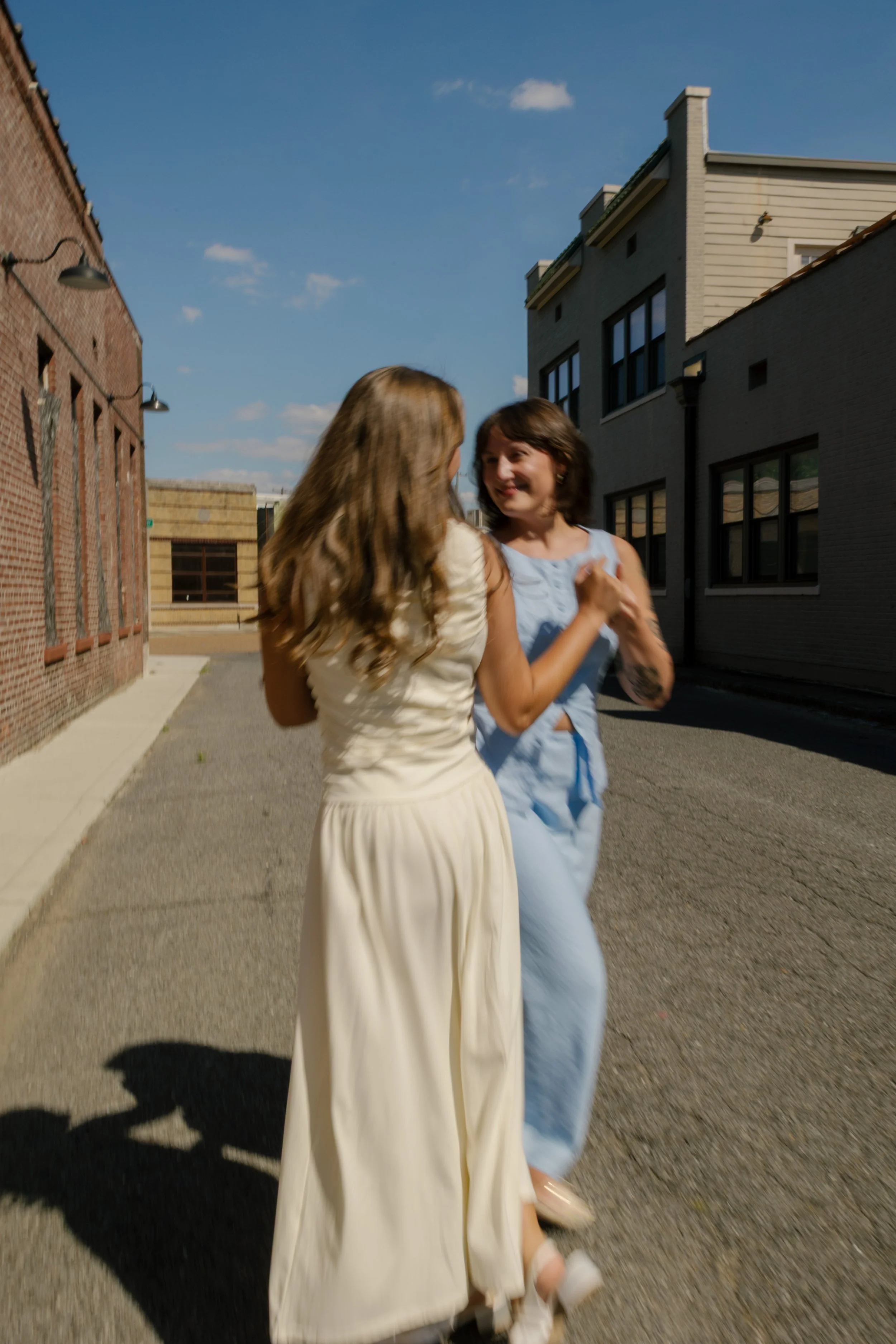 Two brides share a playful dance together on a quiet city street after their wedding ceremony.
