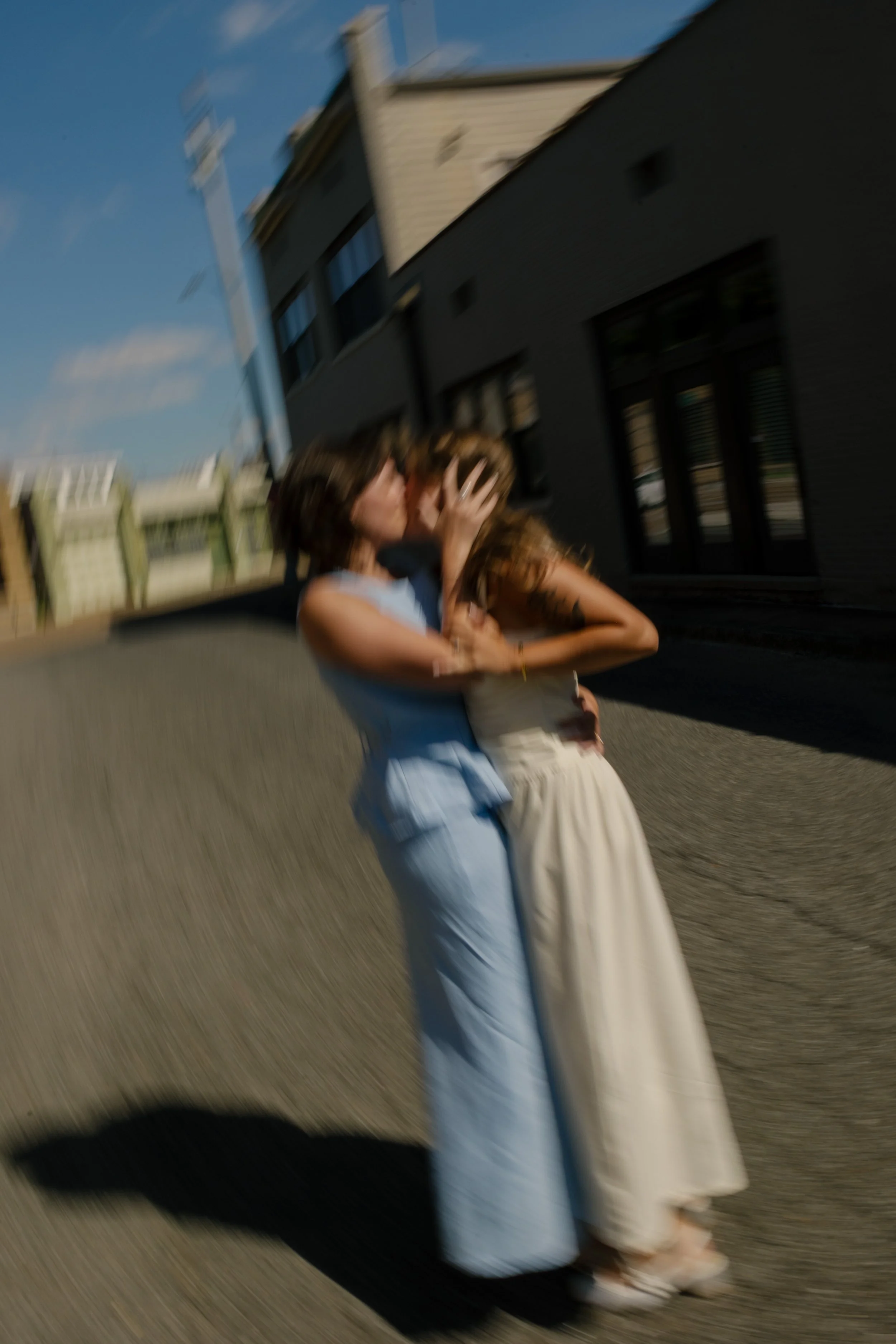 Motion-blur image of two brides embracing in the middle of a quiet city street.