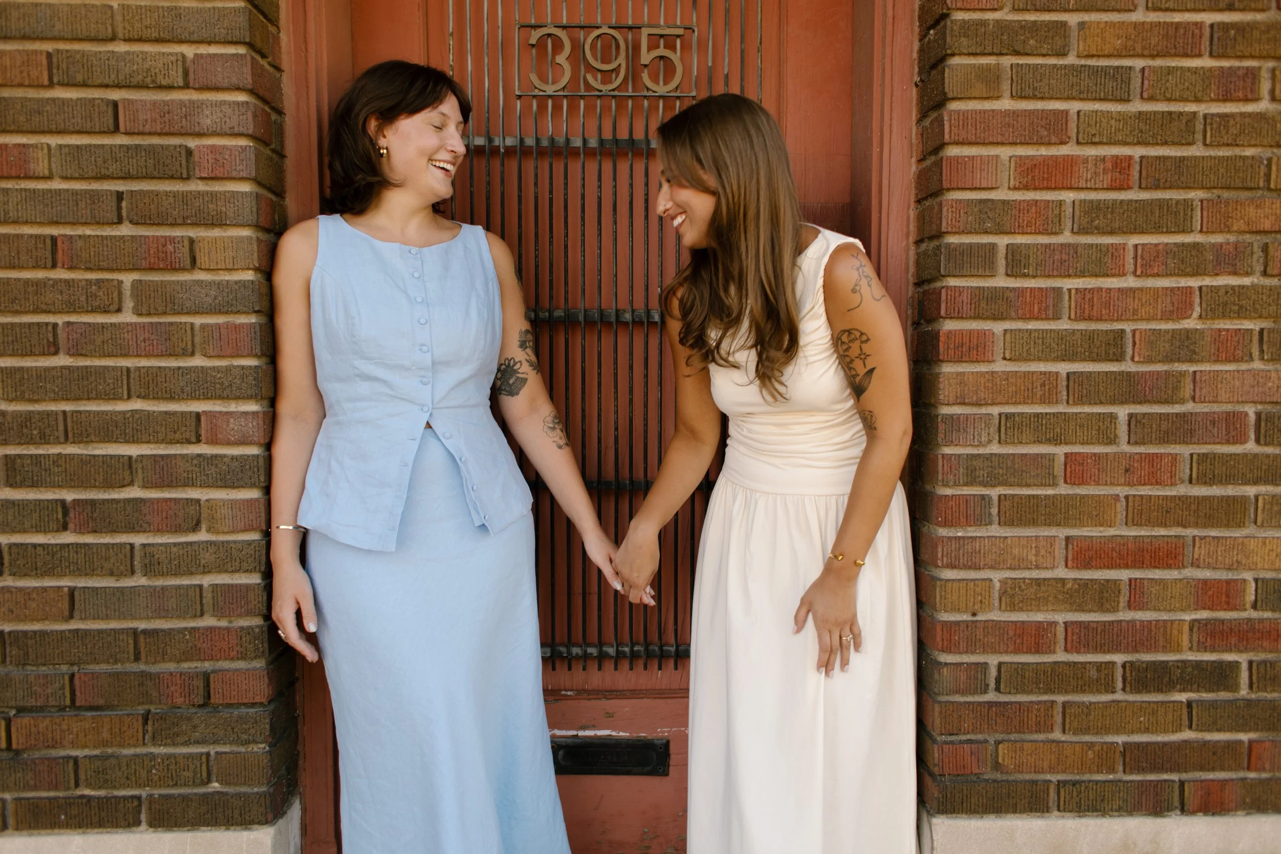 Couple smiles at one another while holding hands in a brick doorway during wedding portraits.