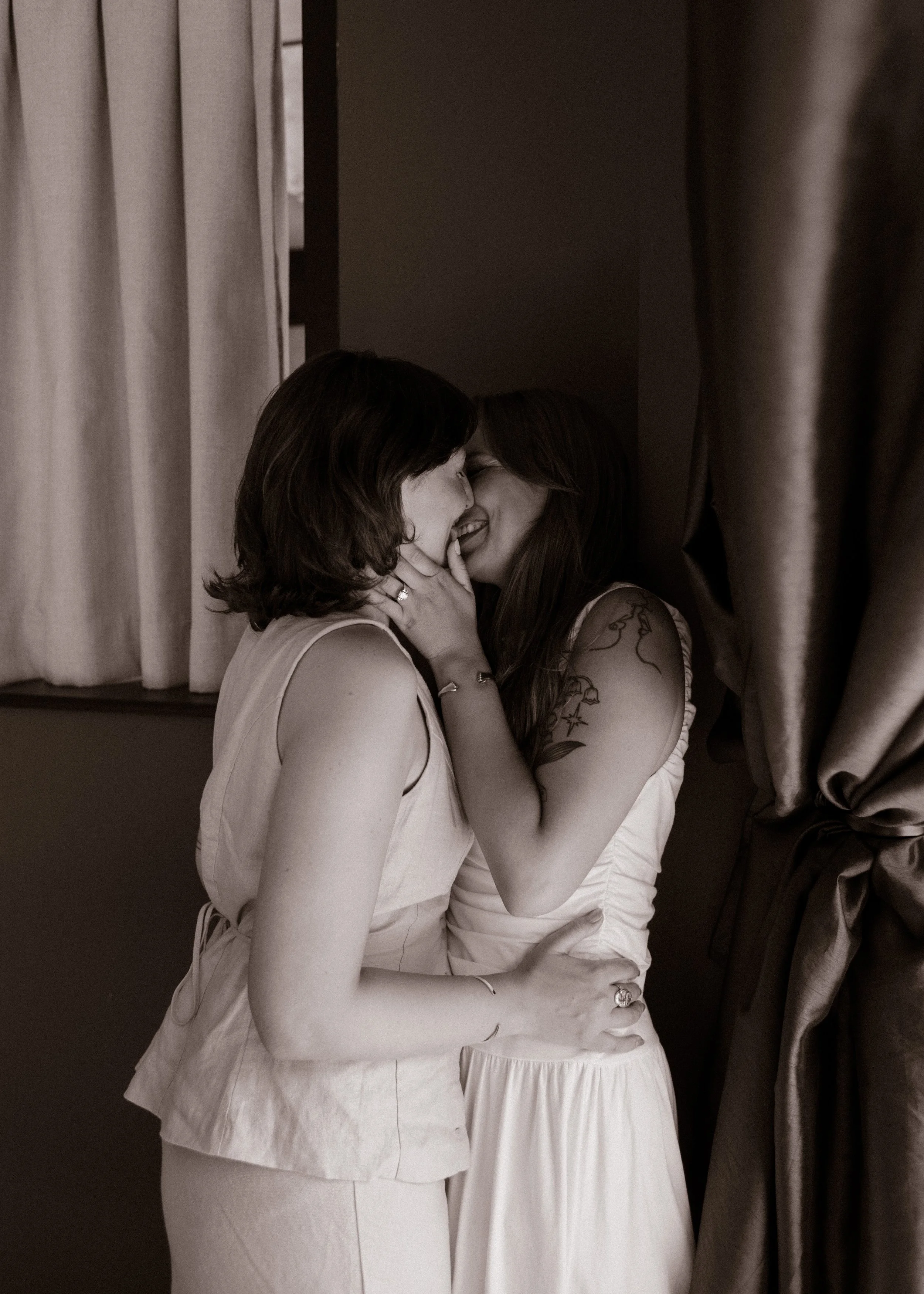 Intimate black-and-white image of two newlyweds sharing a quiet embrace indoors.