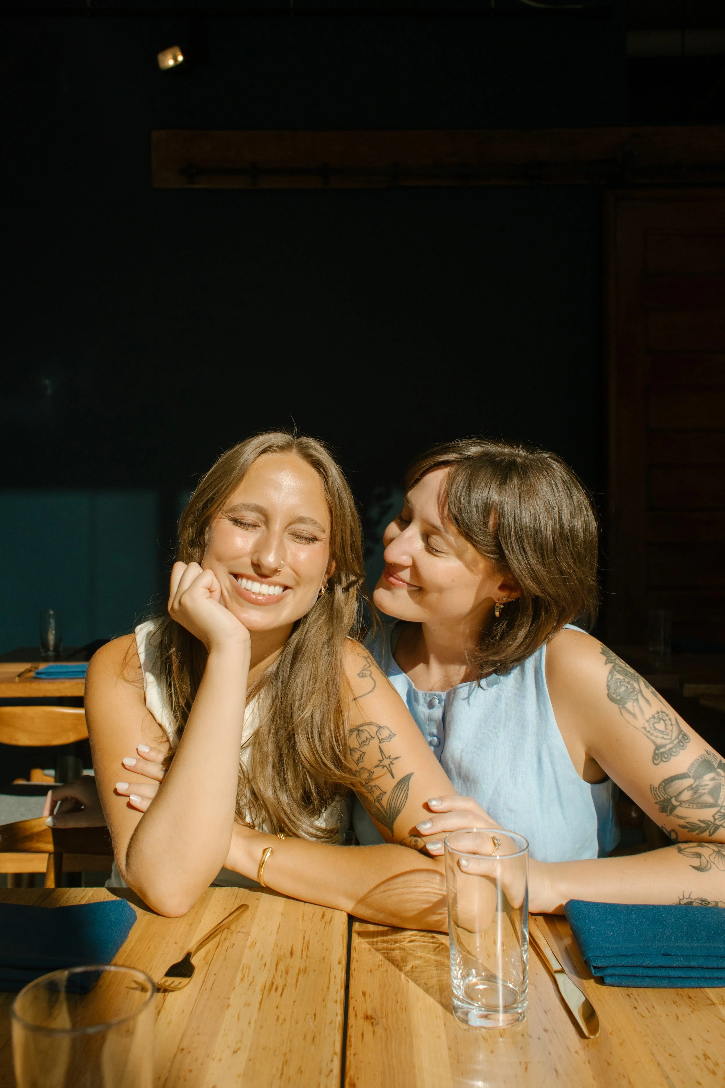 Candid restaurant portrait of one bride smiling as her partner leans in close, captured by a documentary wedding photographer.