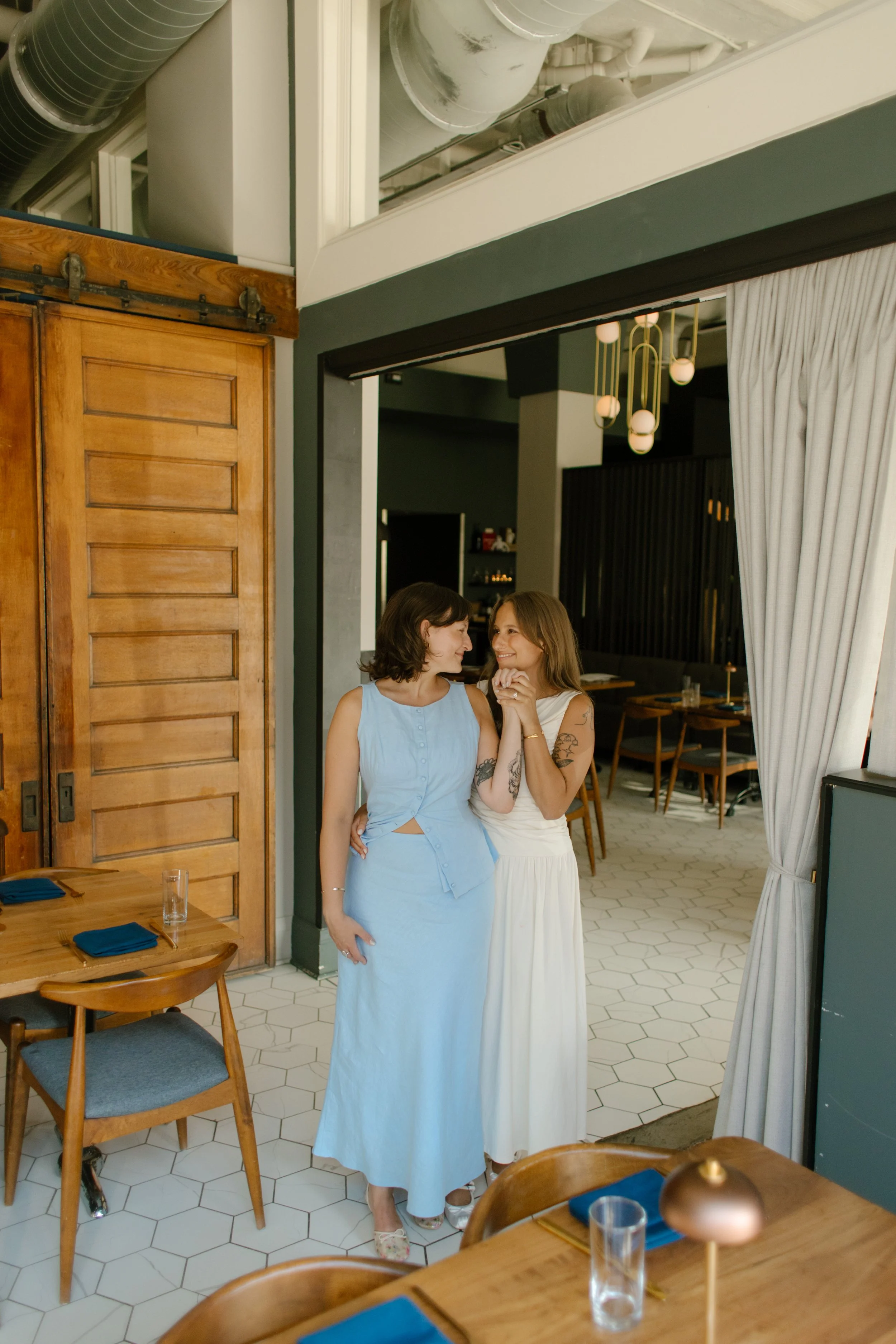 Couple stands together in the doorway of a modern restaurant sharing a quiet laugh.