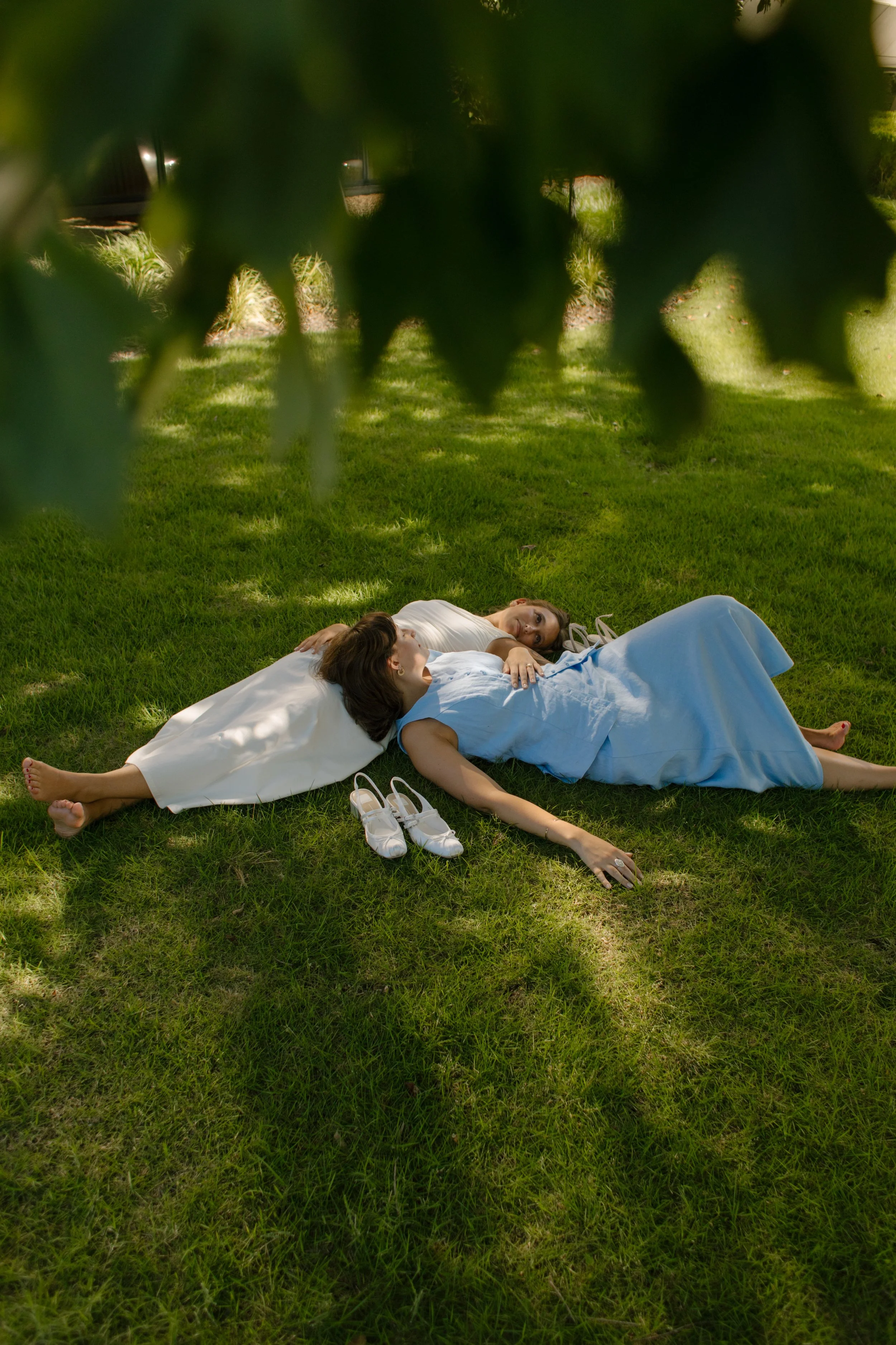 Overhead view of two newlyweds lying together on the grass with their shoes nearby, photographed by a documentary wedding photographer.