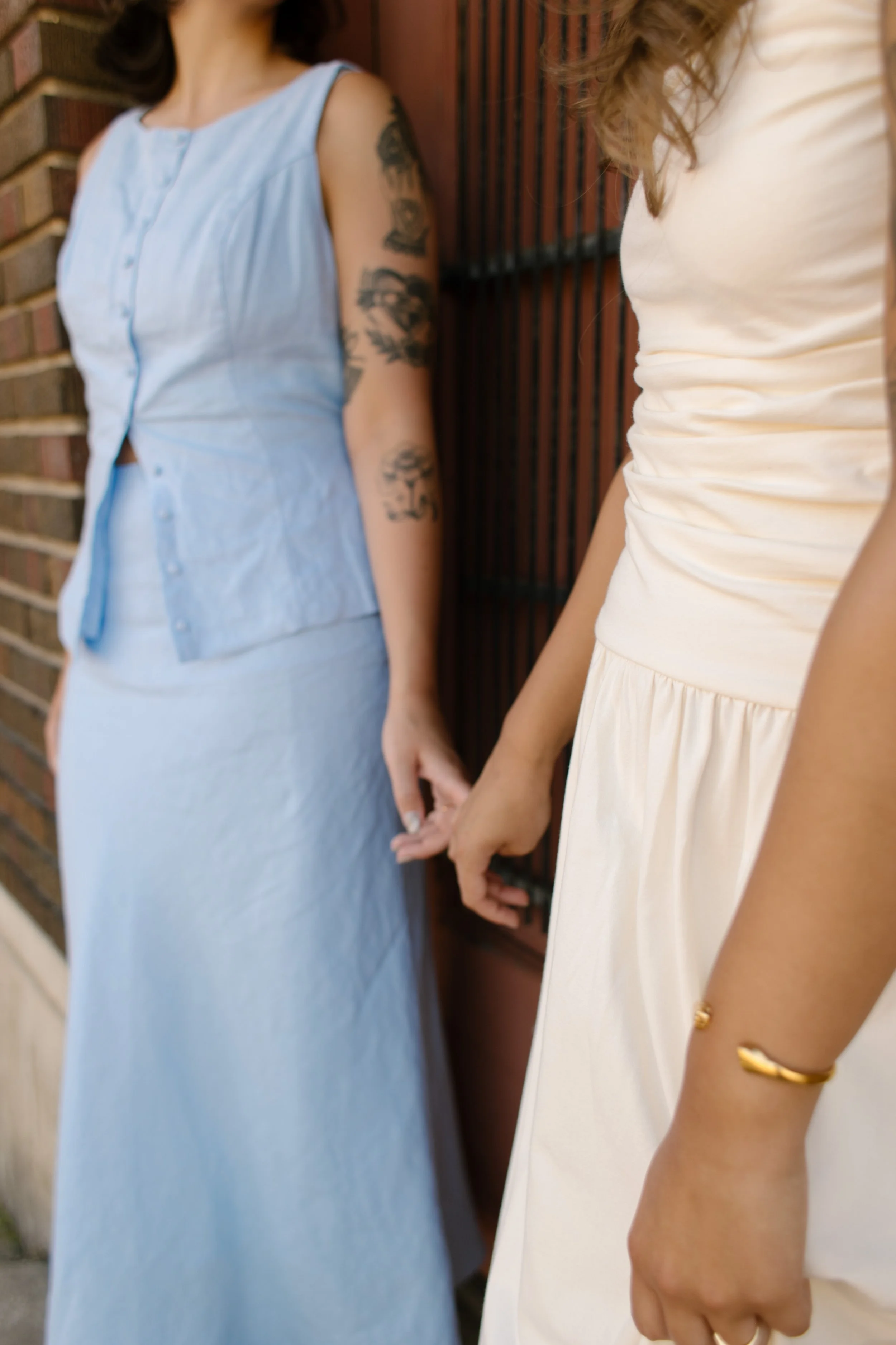 Detail of two brides holding hands outside a brick storefront, photographed by a documentary wedding photographer.
