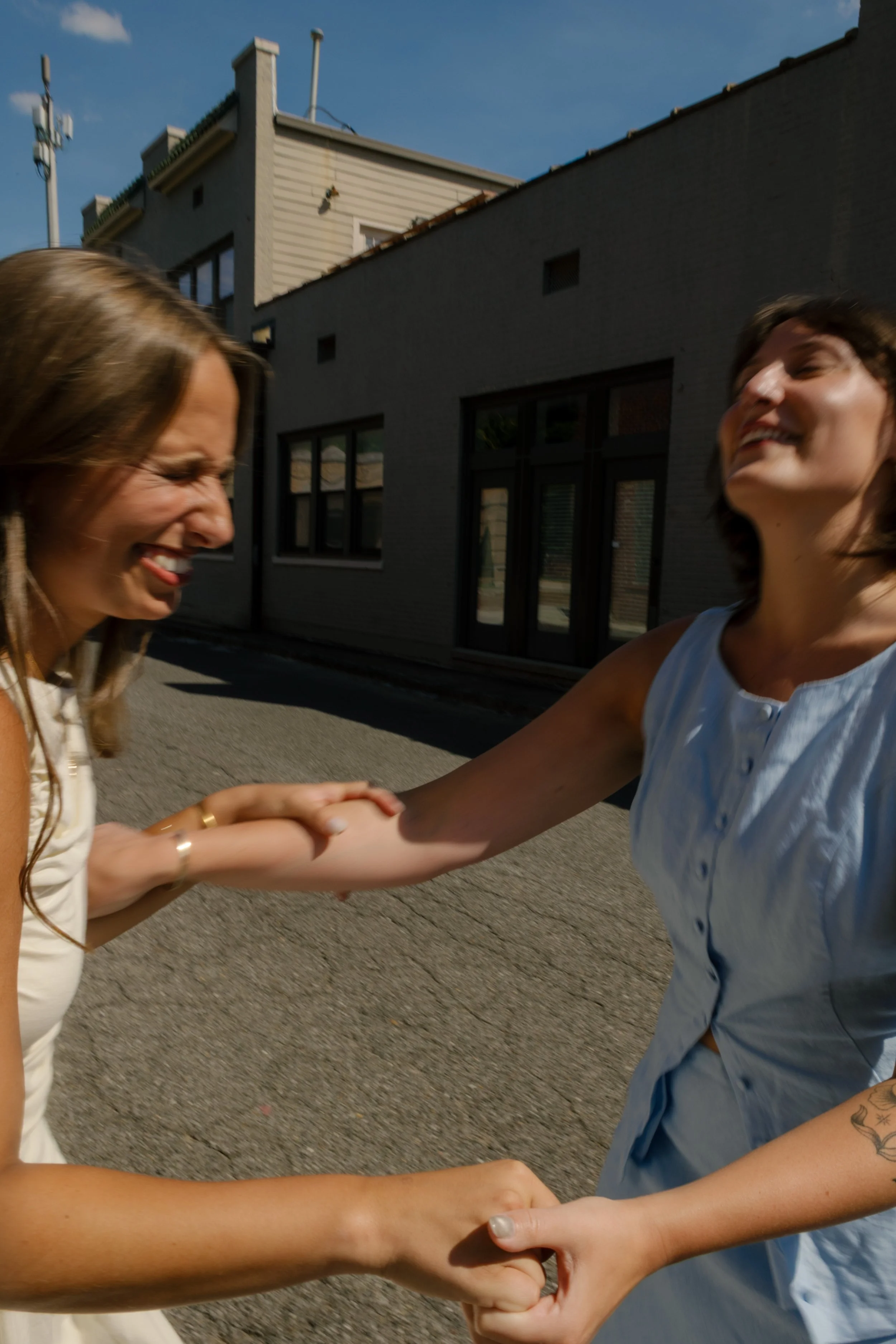 Joyful candid of two newlyweds laughing together while spinning hand in hand on a quiet city street.