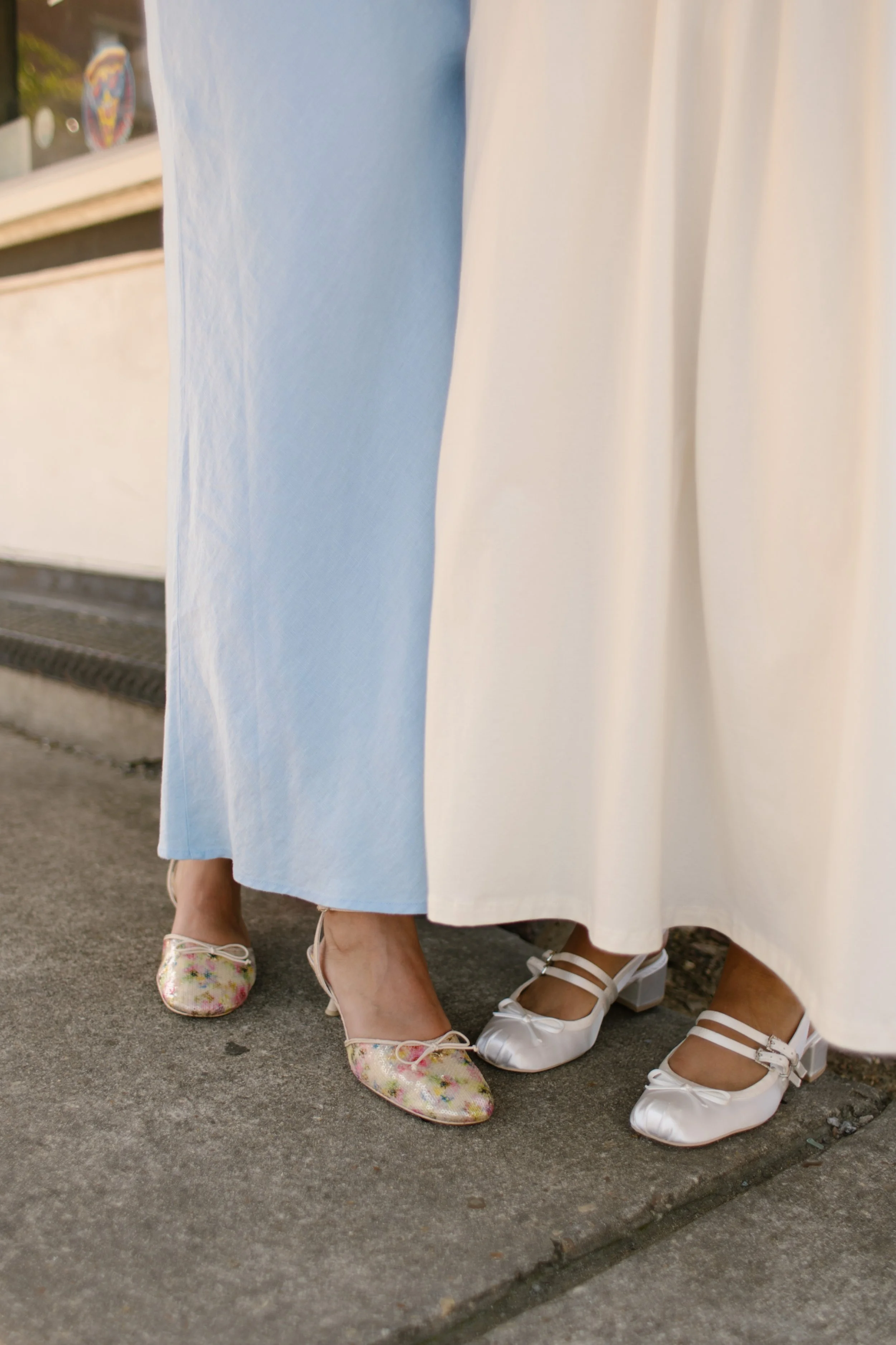 Detail of colorful flats and white wedding shoes standing side by side outside a storefront, photographed by a documentary wedding photographer.