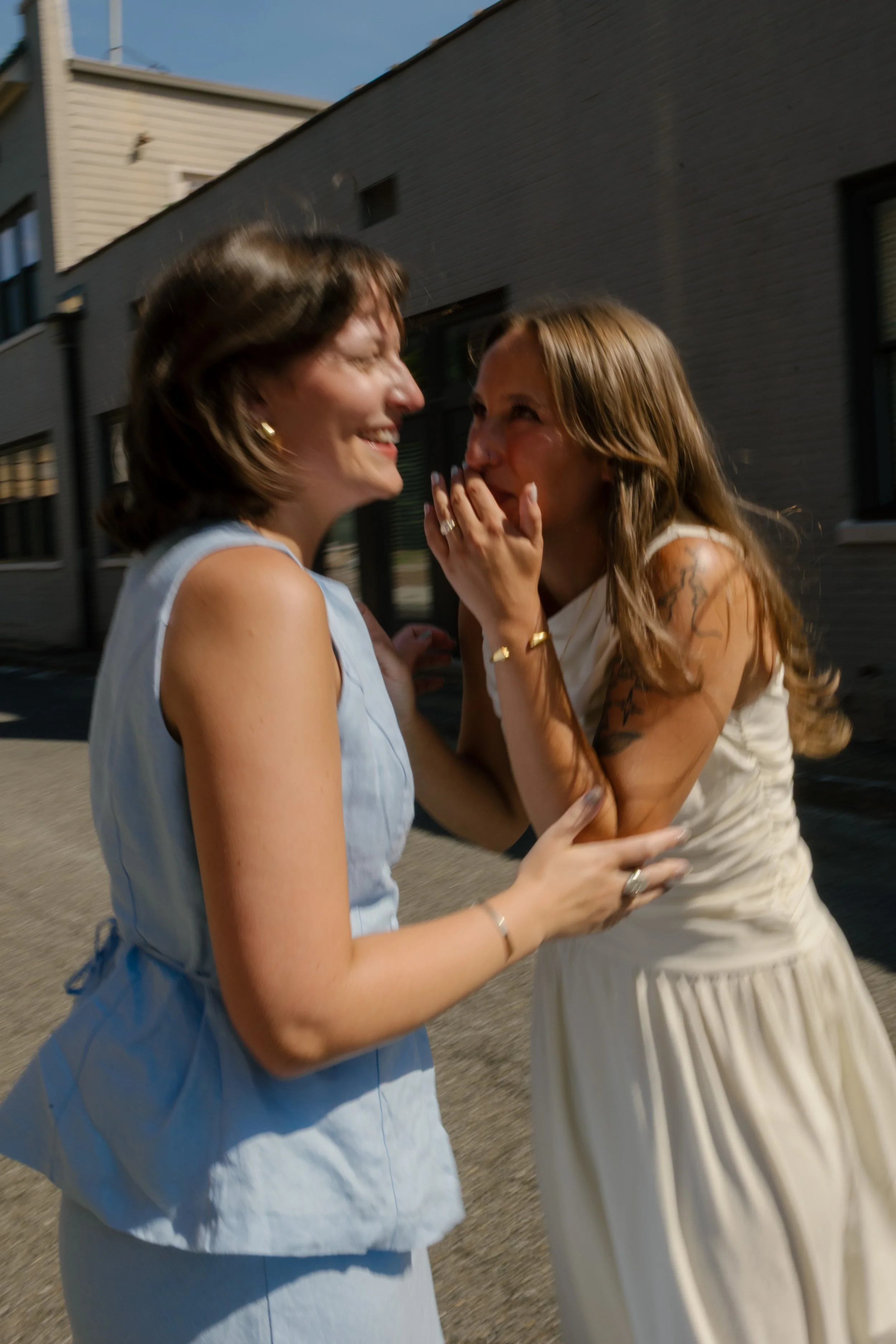 Two brides laugh together on a quiet city street during candid portraits by a documentary wedding photographer.
