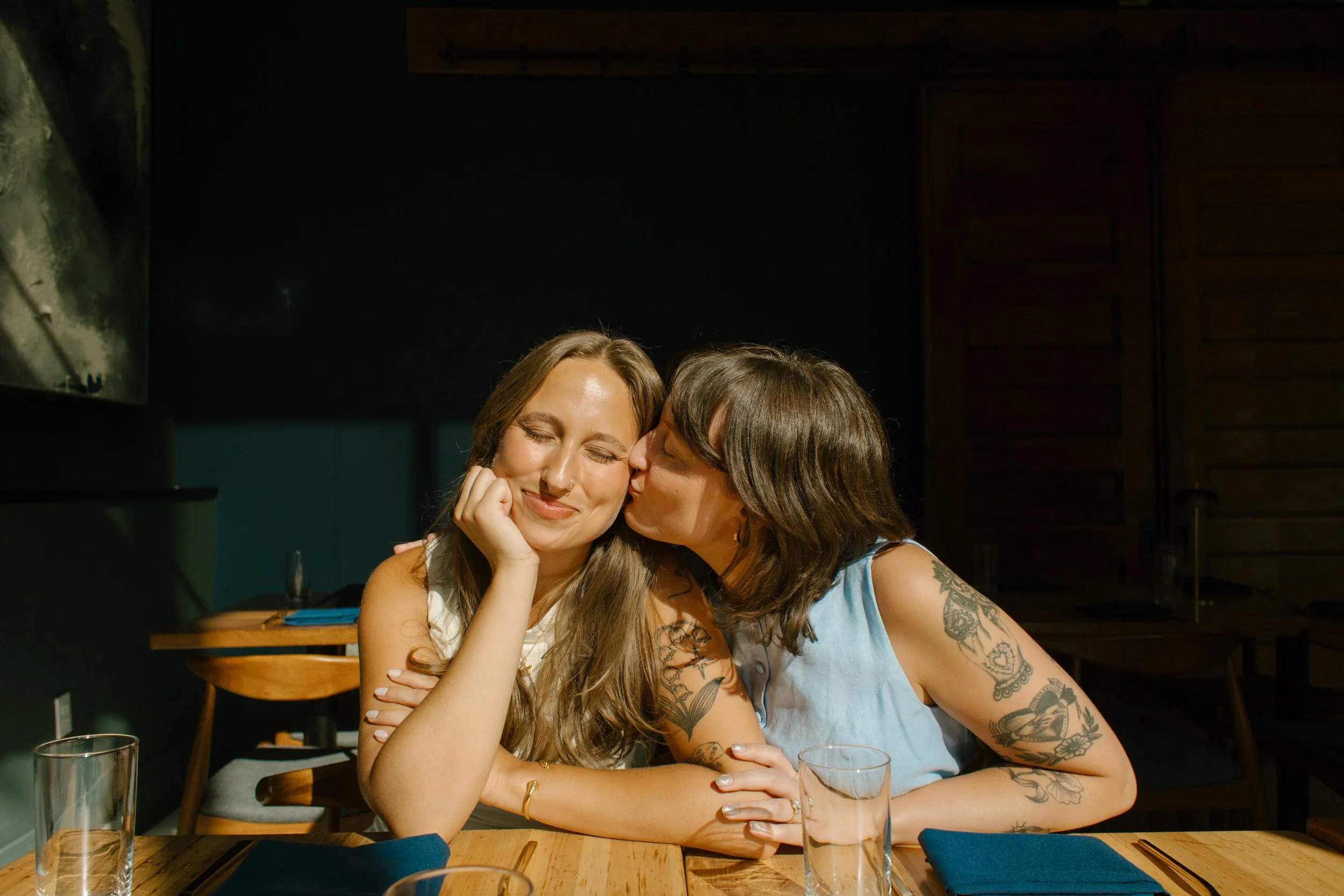 Close-up of two brides embracing in front of a glass block wall during intimate wedding portraits.
