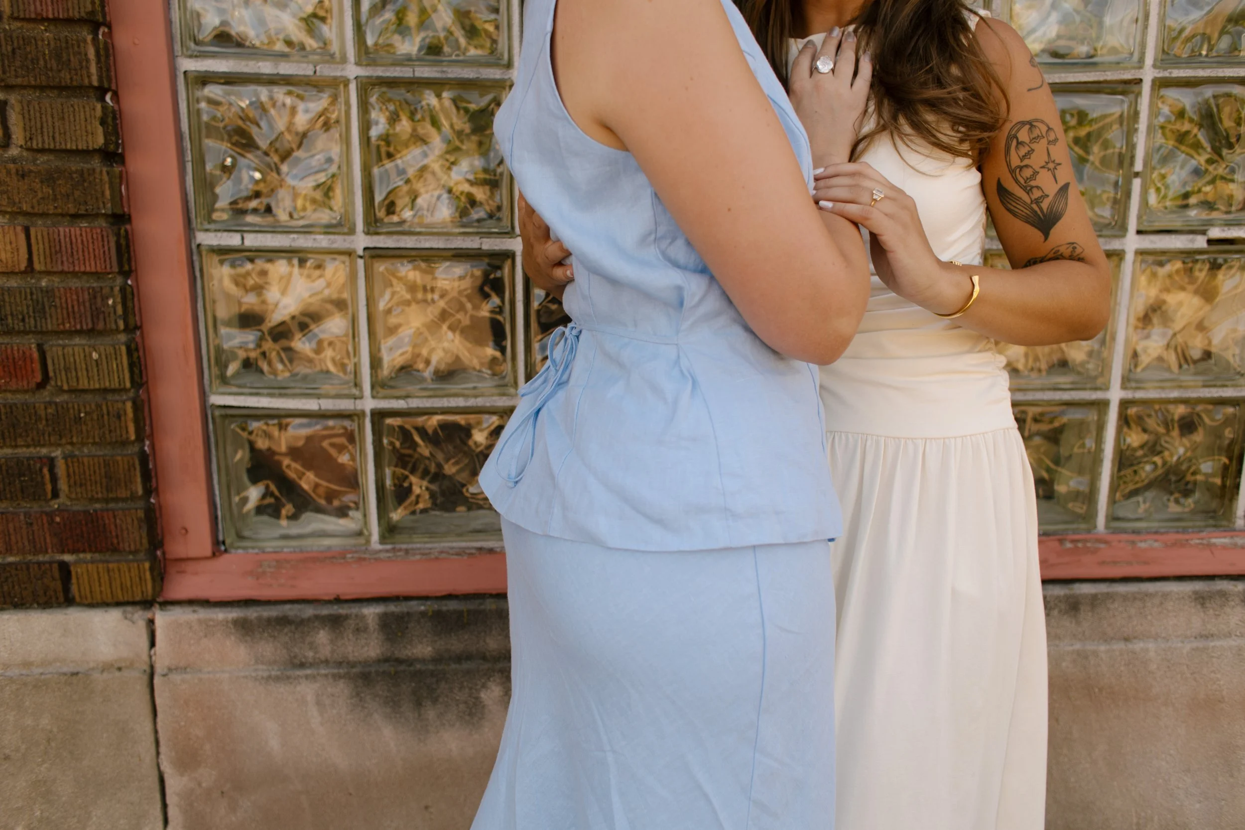 Close-up of two brides embracing in front of a glass block wall during intimate wedding portraits.