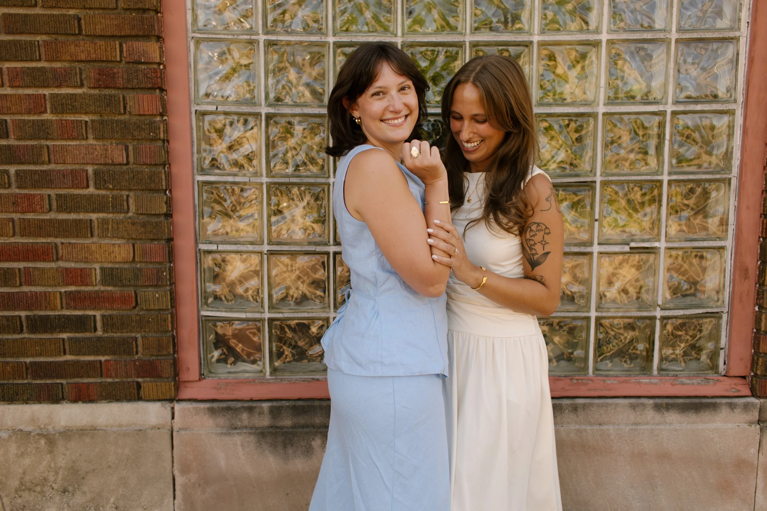 Couple smiles together against a glass block wall during relaxed documentary-style wedding photography.