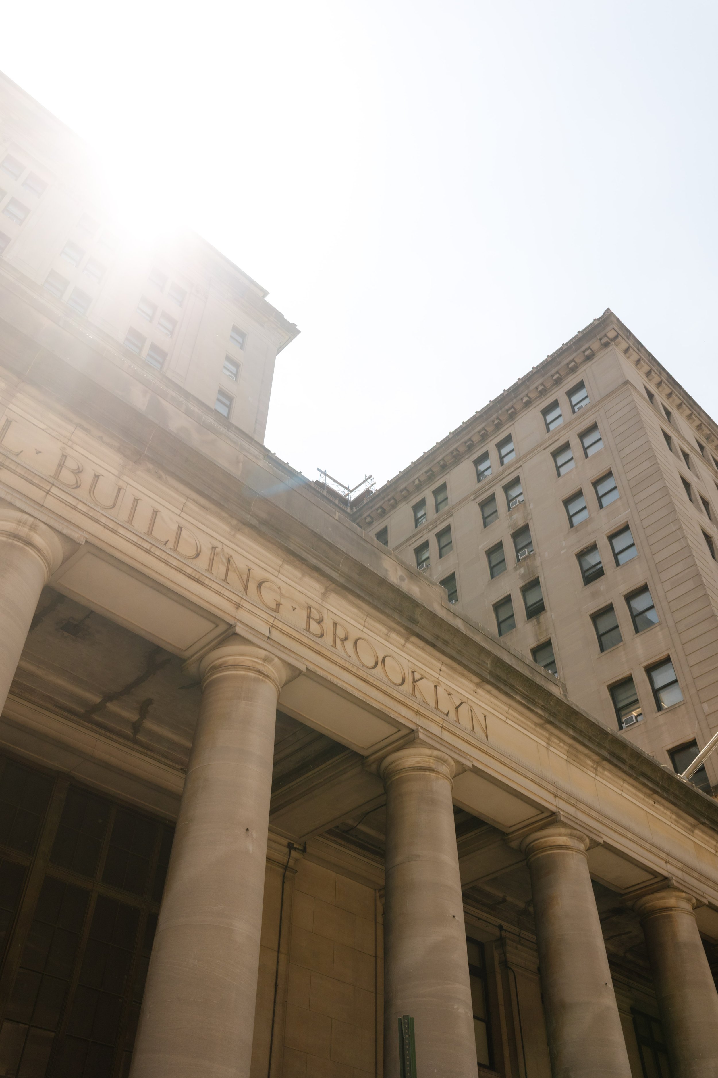 Sunlit architectural view of the Brooklyn Municipal Building, featuring its grand stone columns.