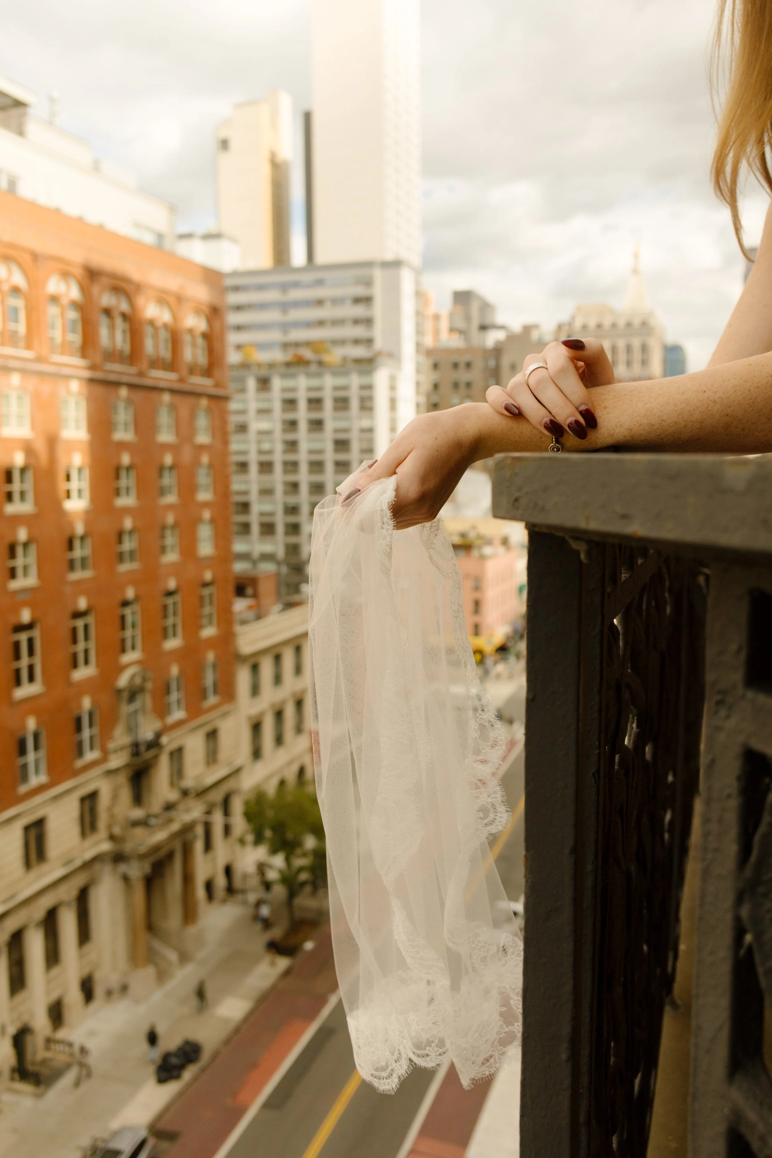 Bride holding a lace veil over a balcony with New York City streets and architecture in the background.