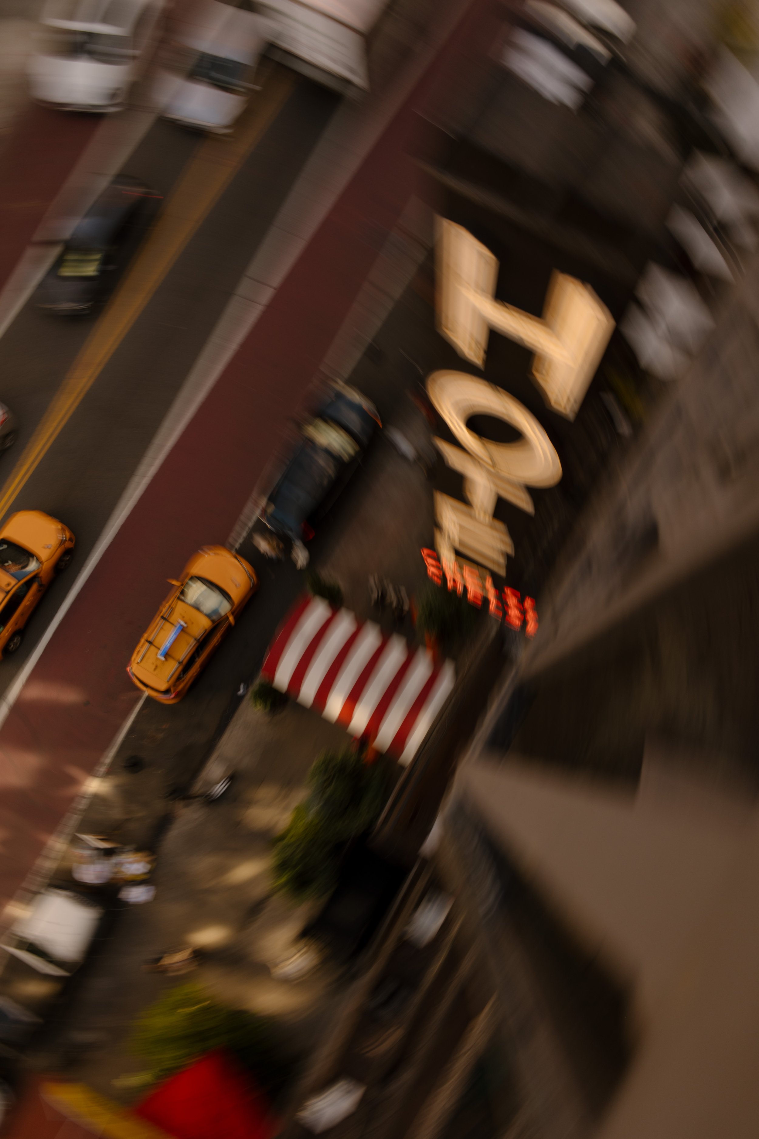 Motion-blurred view of yellow taxis and a hotel entrance on a busy NYC street.