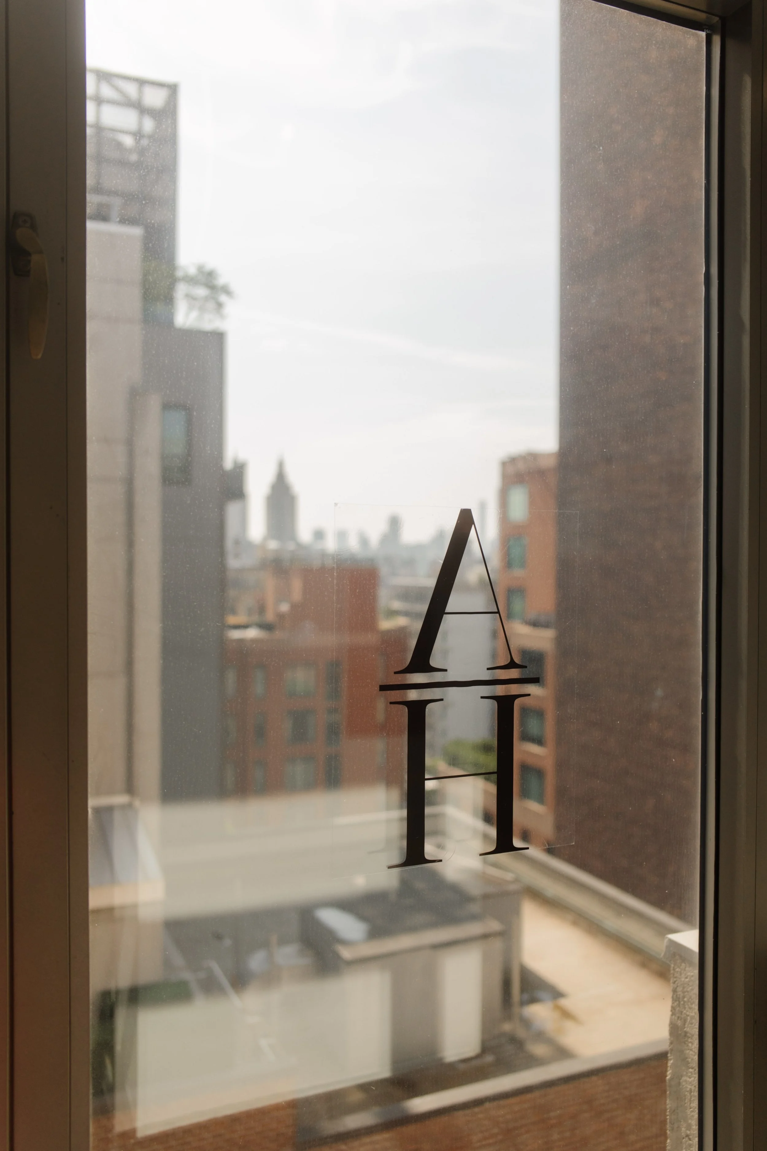 Hotel window detail with monogram lettering and a softly focused New York City skyline beyond.
