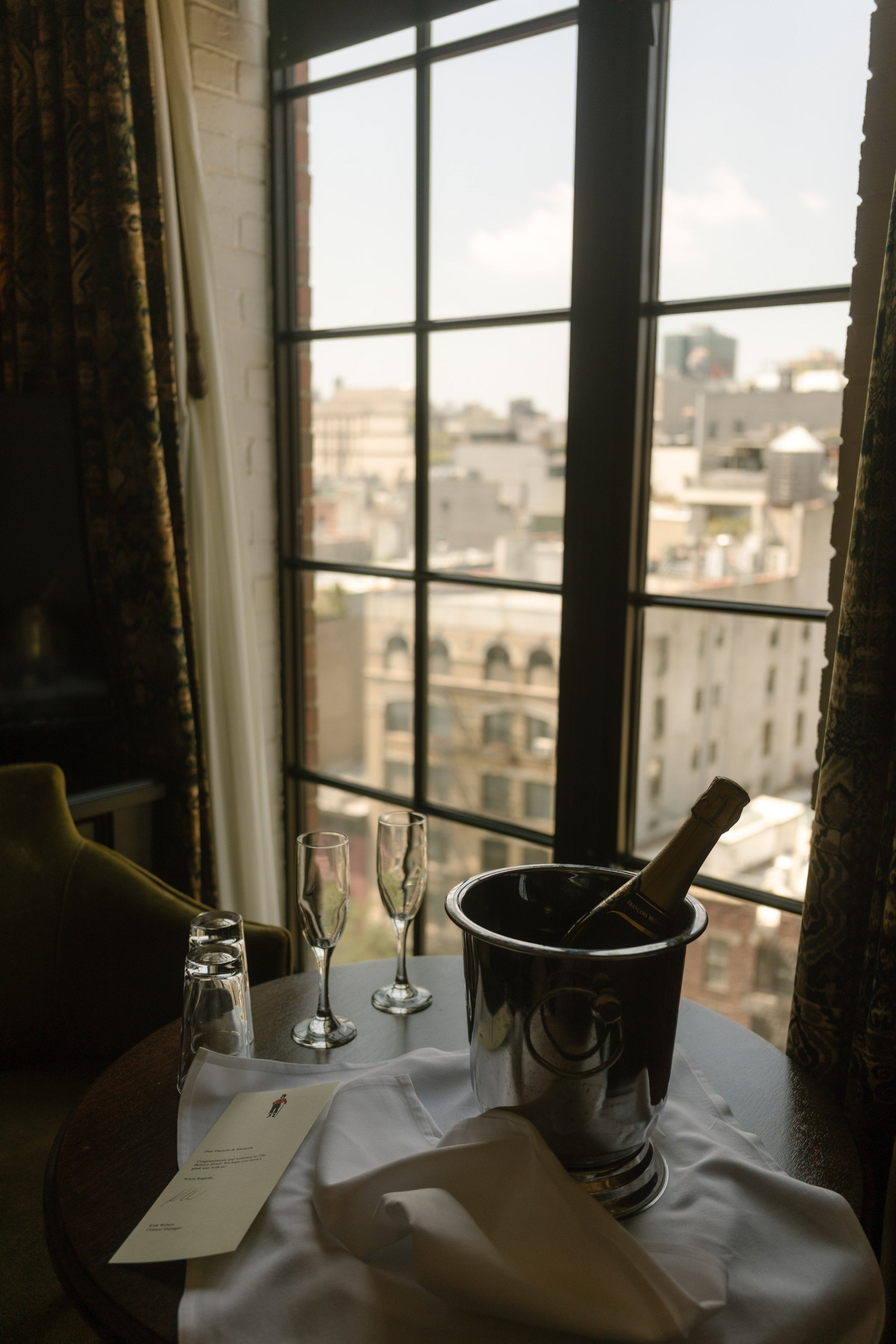 Champagne, glasses and an ice bucket beside a hotel window overlooking the New York City skyline.