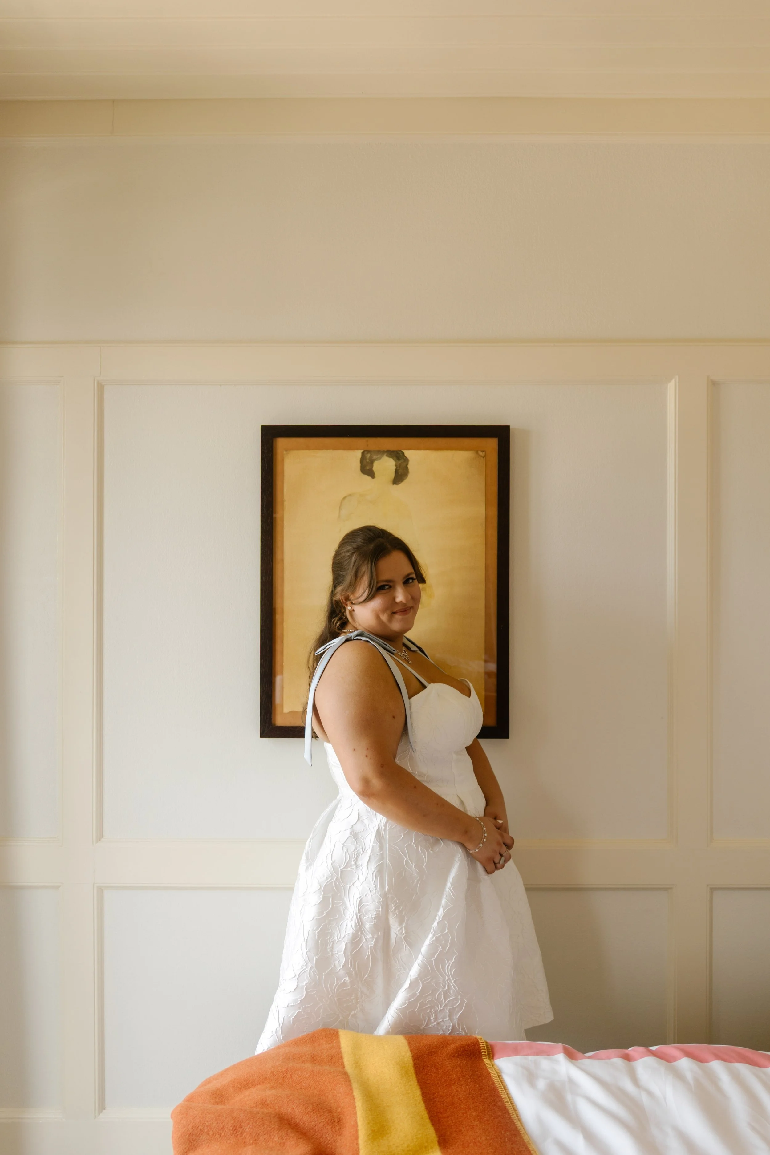Bride posing in her wedding dress inside a warmly lit NYC hotel room.