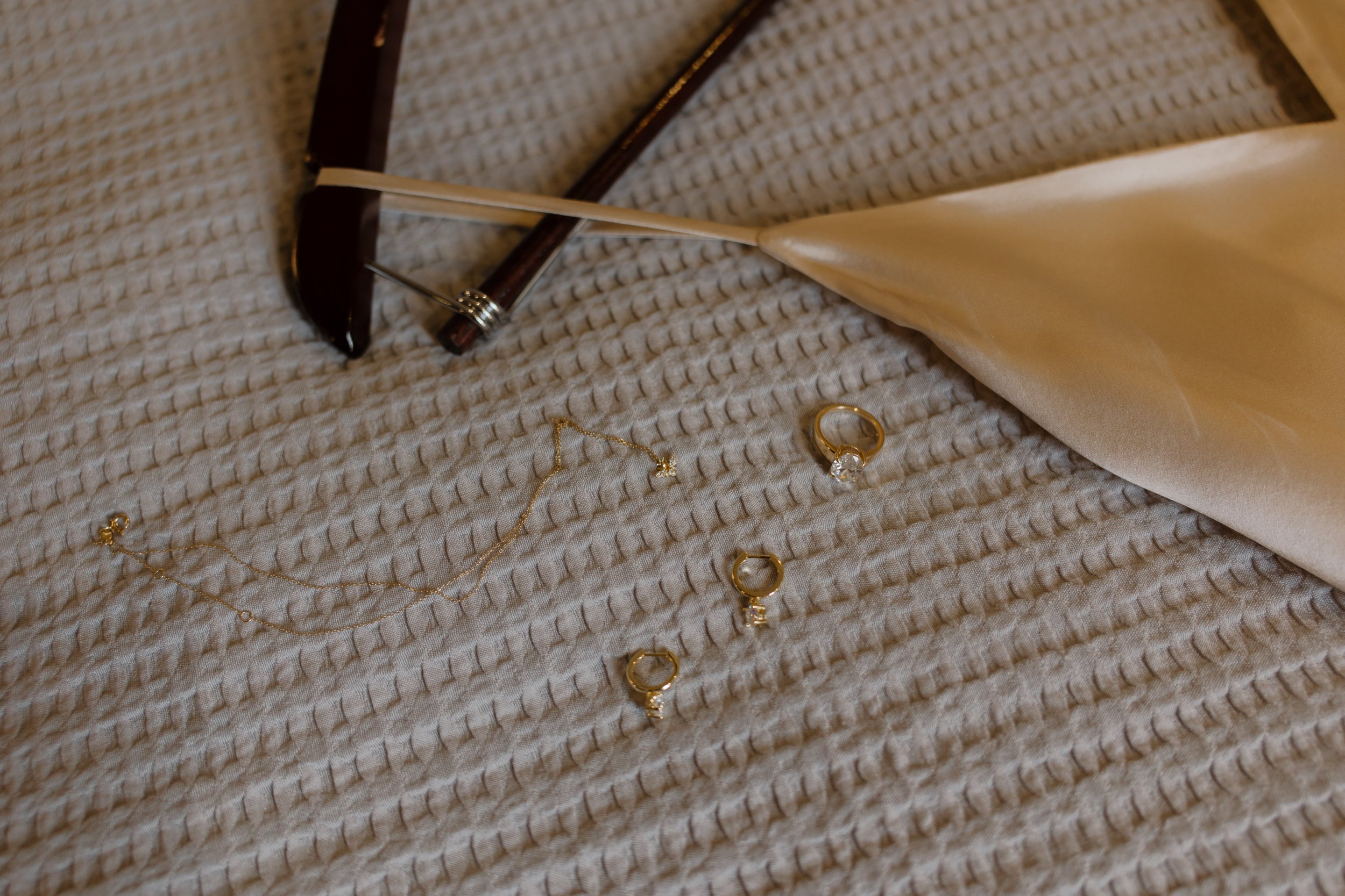 Wedding jewelry and accessories arranged on a textured bedspread before a New York City wedding.