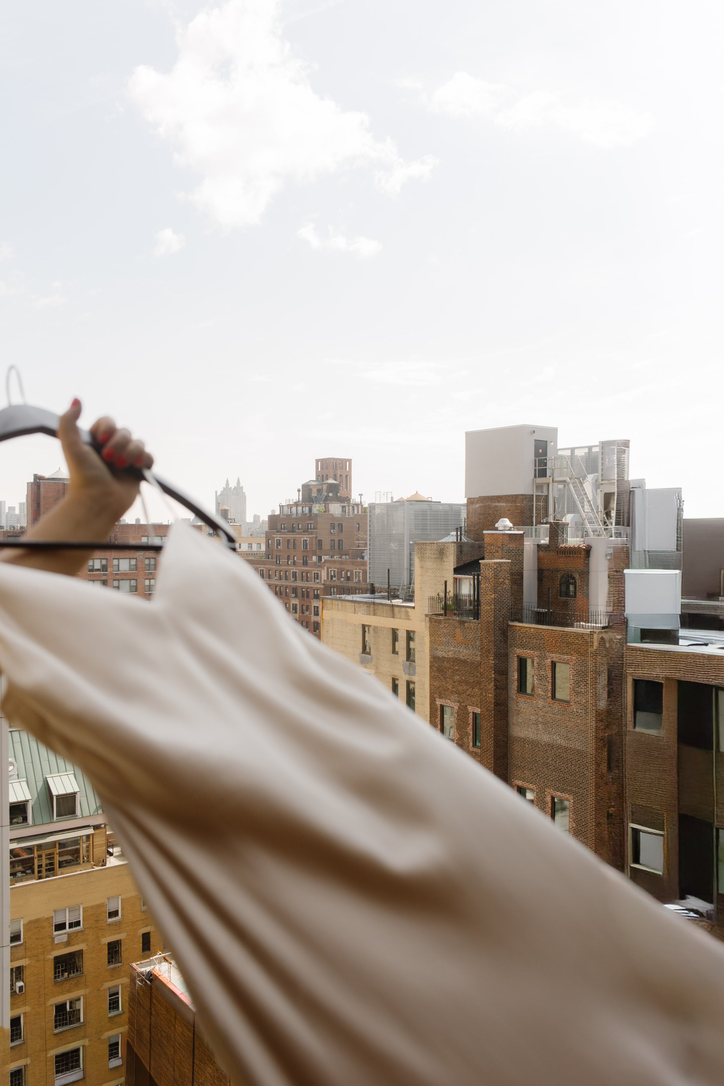 Wedding dress held in front of a hotel window overlooking the NYC skyline.