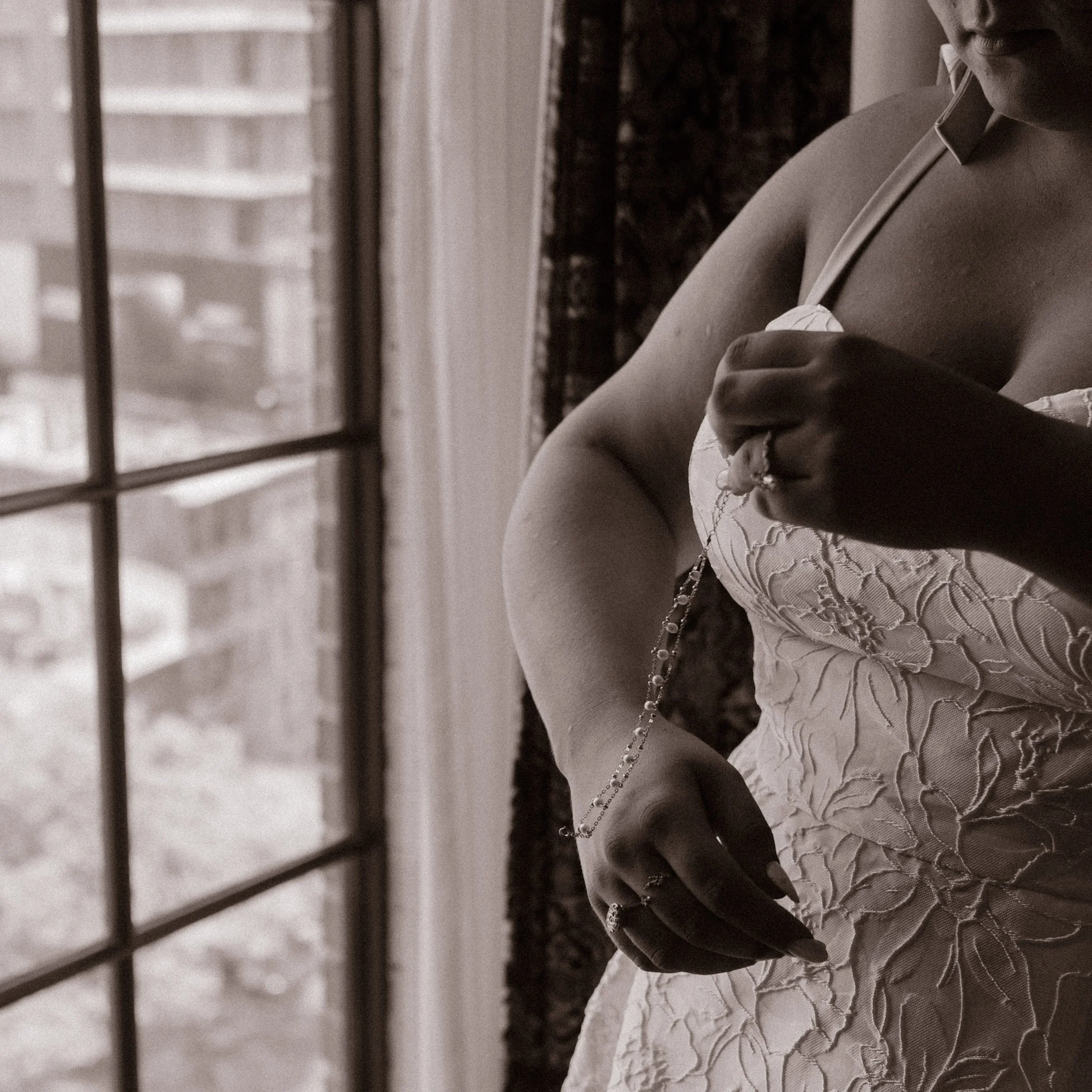 Black-and-white detail of a bride fastening delicate jewelry while getting ready for her wedding.