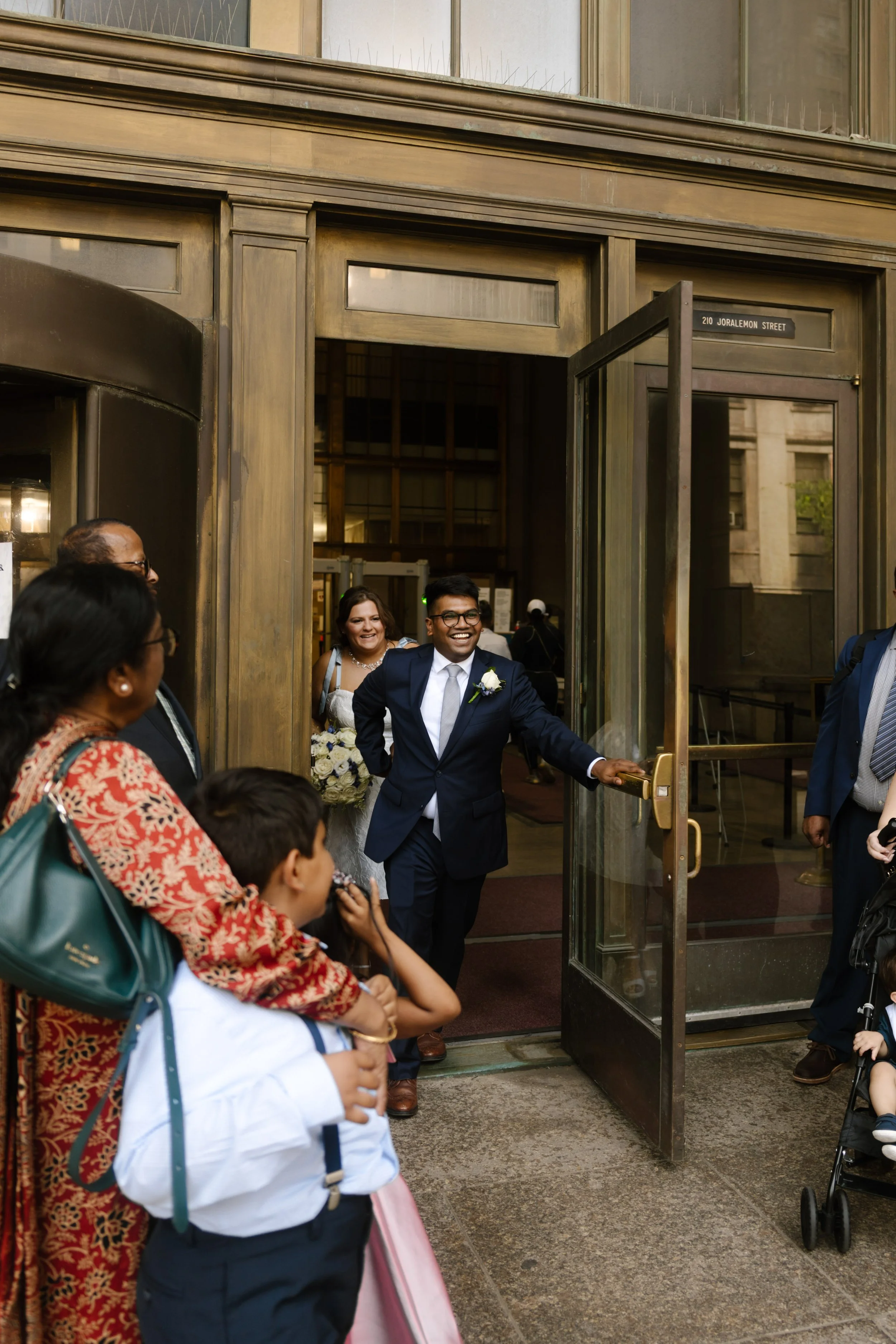 Newlyweds smiling as they exit a New York City building surrounded by family and wedding guests near NYC hotels.