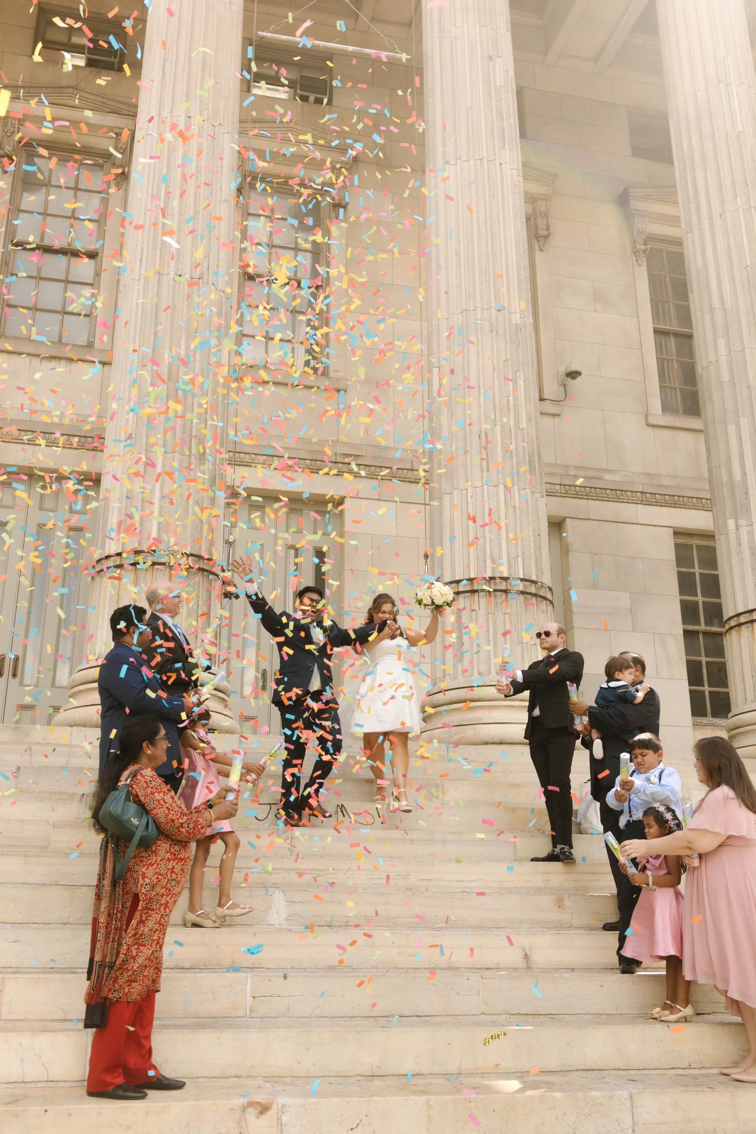 Newlyweds walking through a shower of colorful confetti after their NYC courthouse wedding.