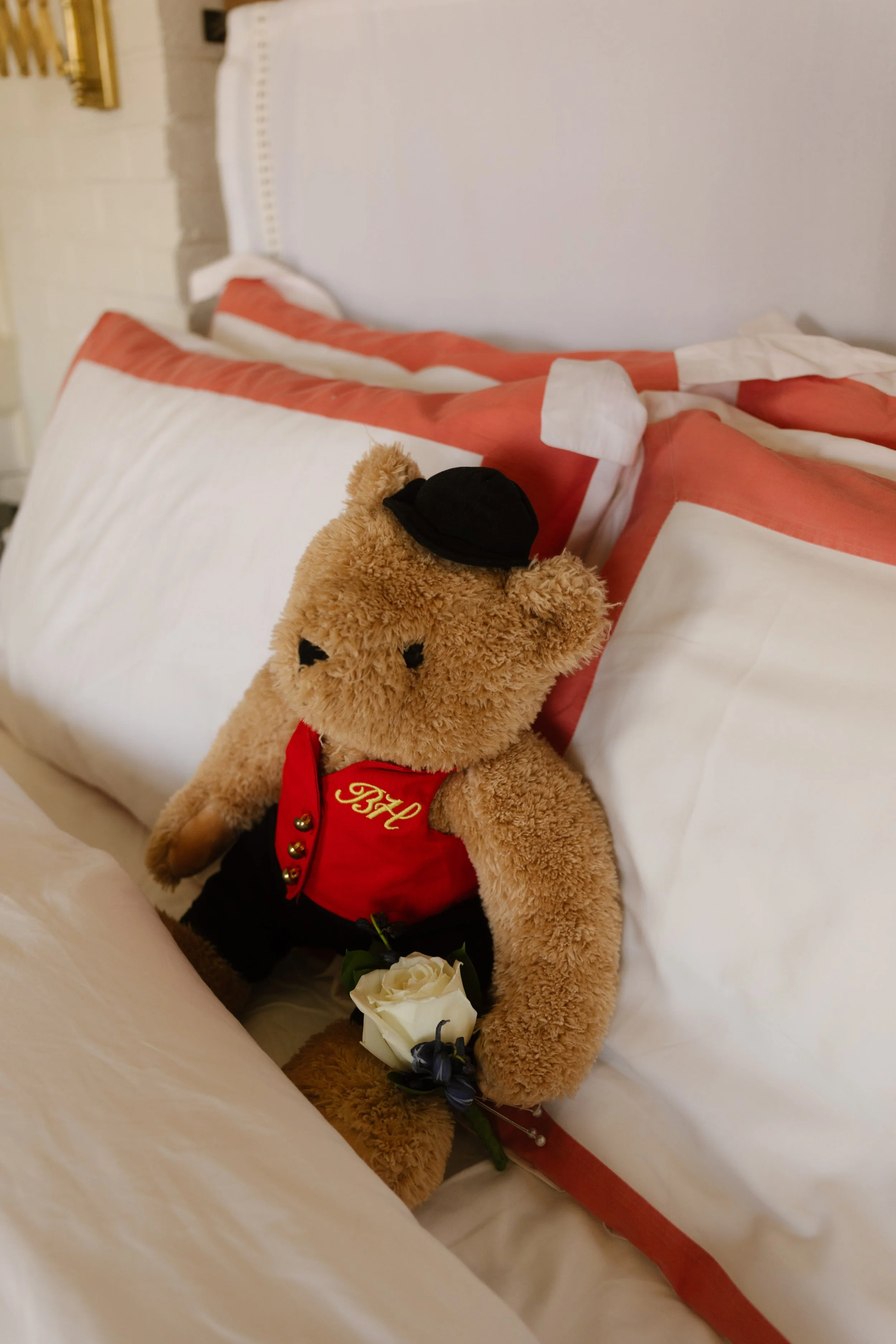 Bowery Hotel teddy bear dressed in a red vest and bowler hat sitting on a hotel bed.