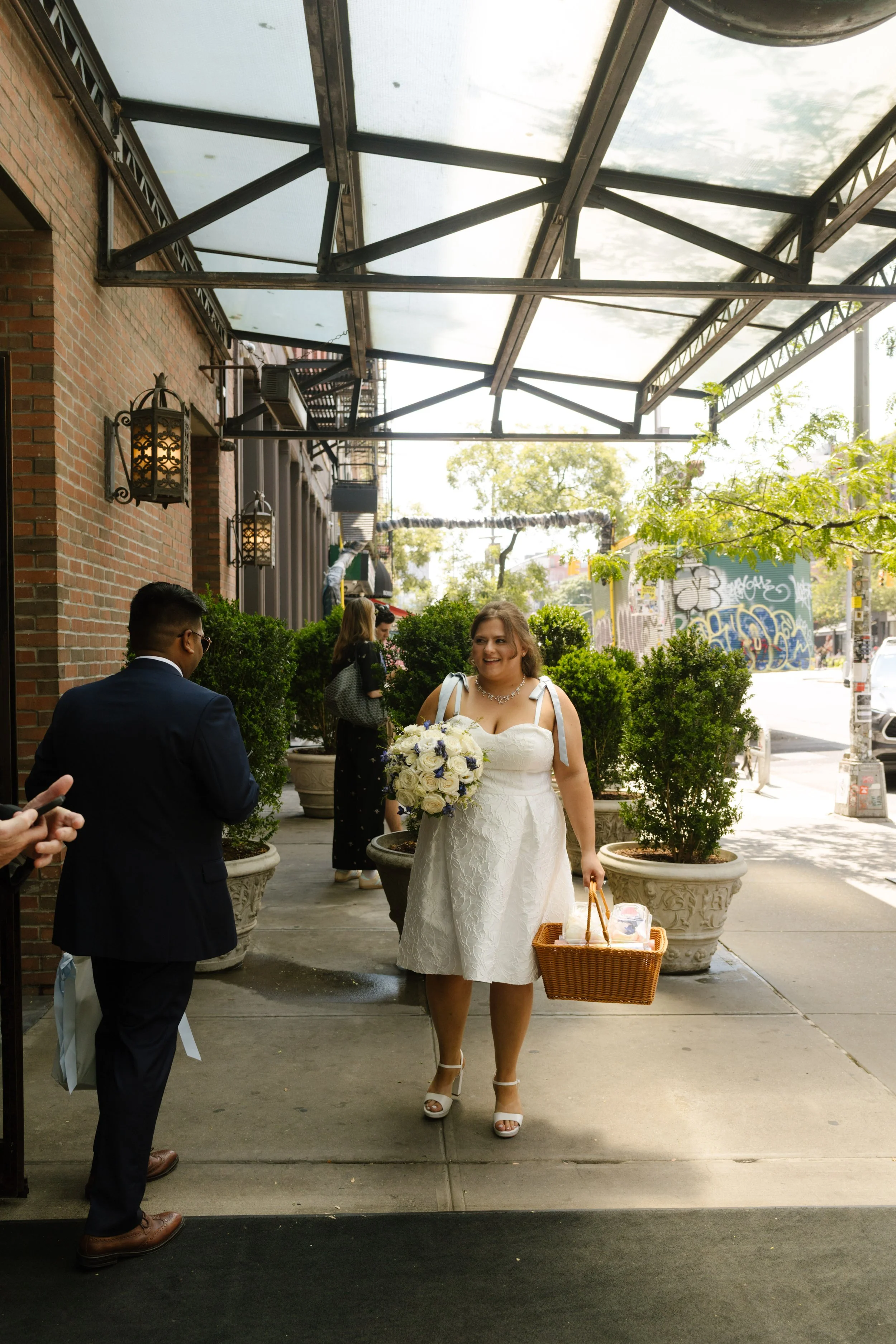 Bride carrying a white floral bouquet and basket outside one of the NYC hotels before her wedding.