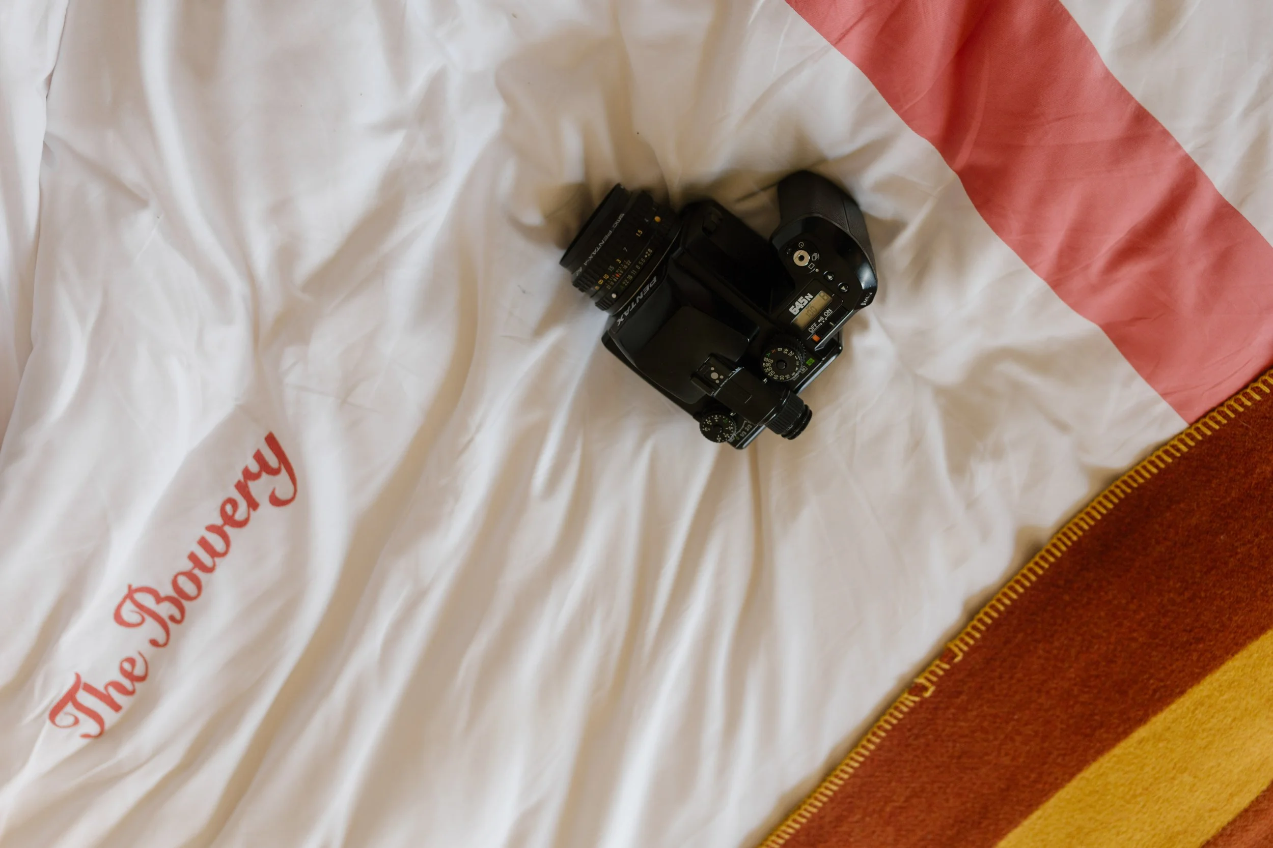 Vintage camera resting on white Bowery Hotel bedding with red accents.