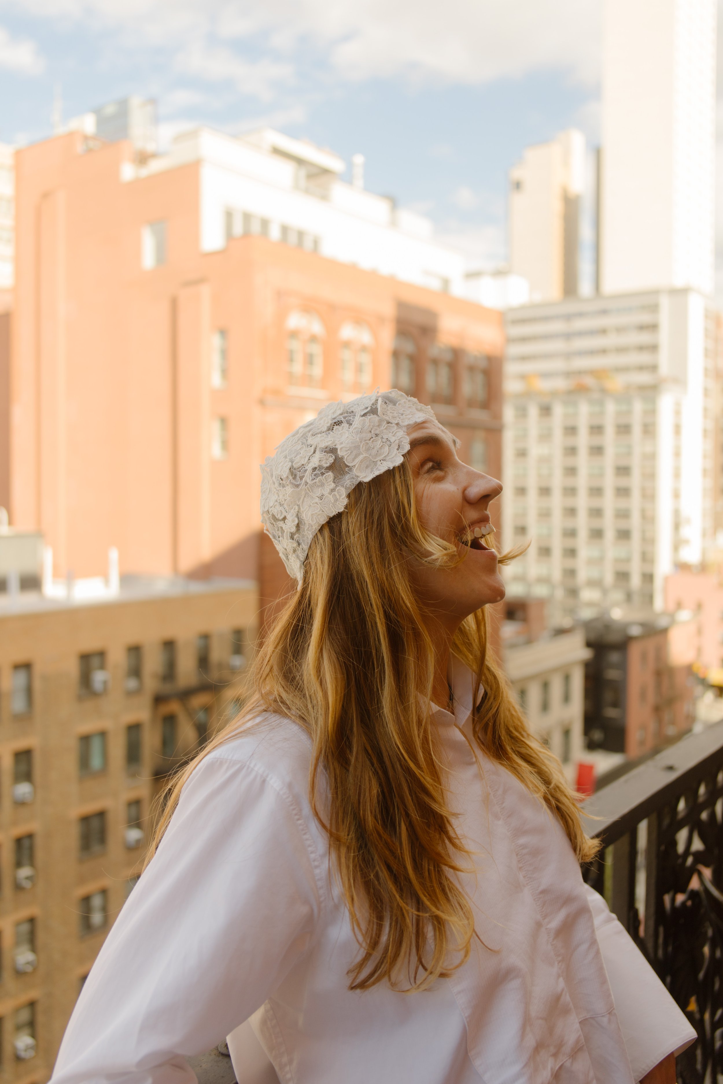 Bride smiles on a hotel balcony while trying on her lace headpiece at one of the charming NYC hotels.