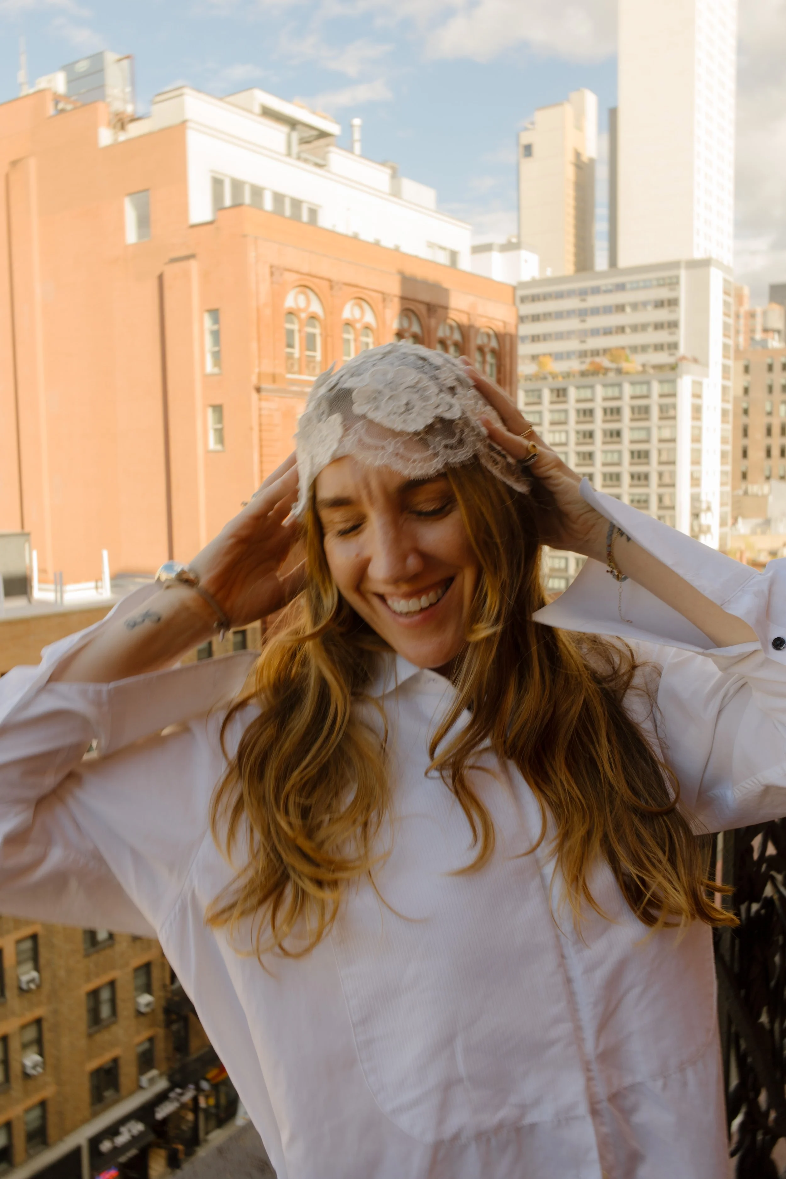 Bride laughs while adjusting her lace bridal headpiece on the balcony of one of the beautiful NYC hotels before the ceremony.