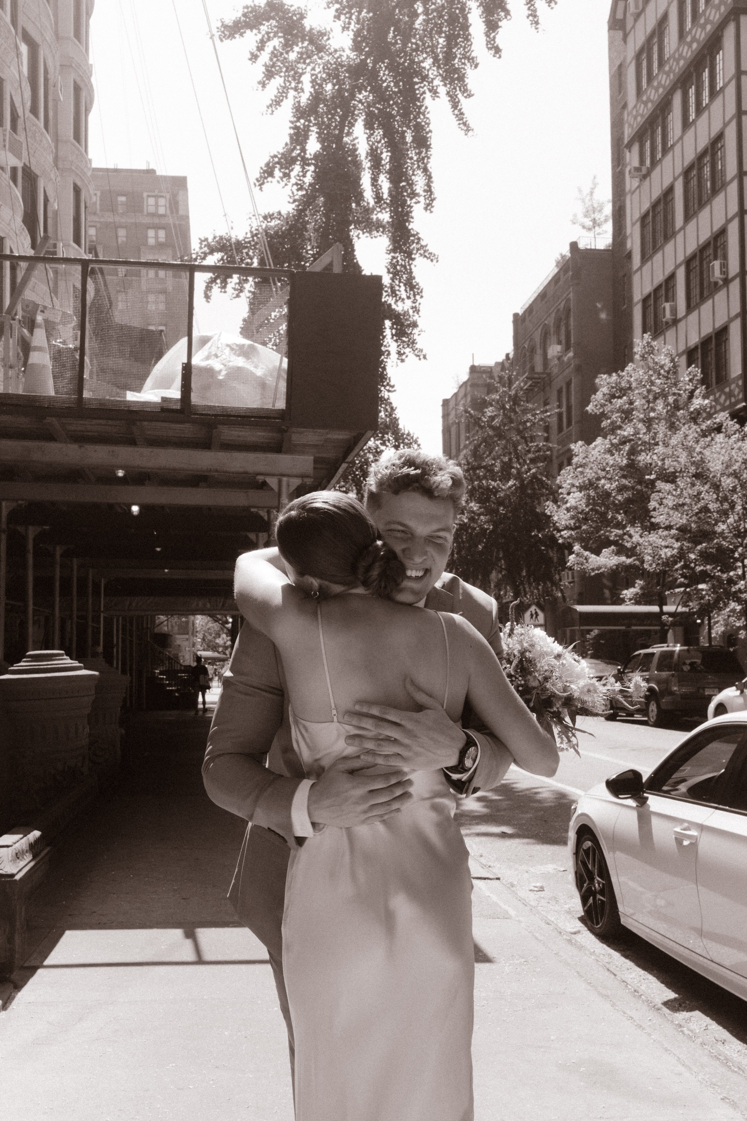 Black-and-white photo of newlyweds embracing and smiling on a New York City sidewalk.