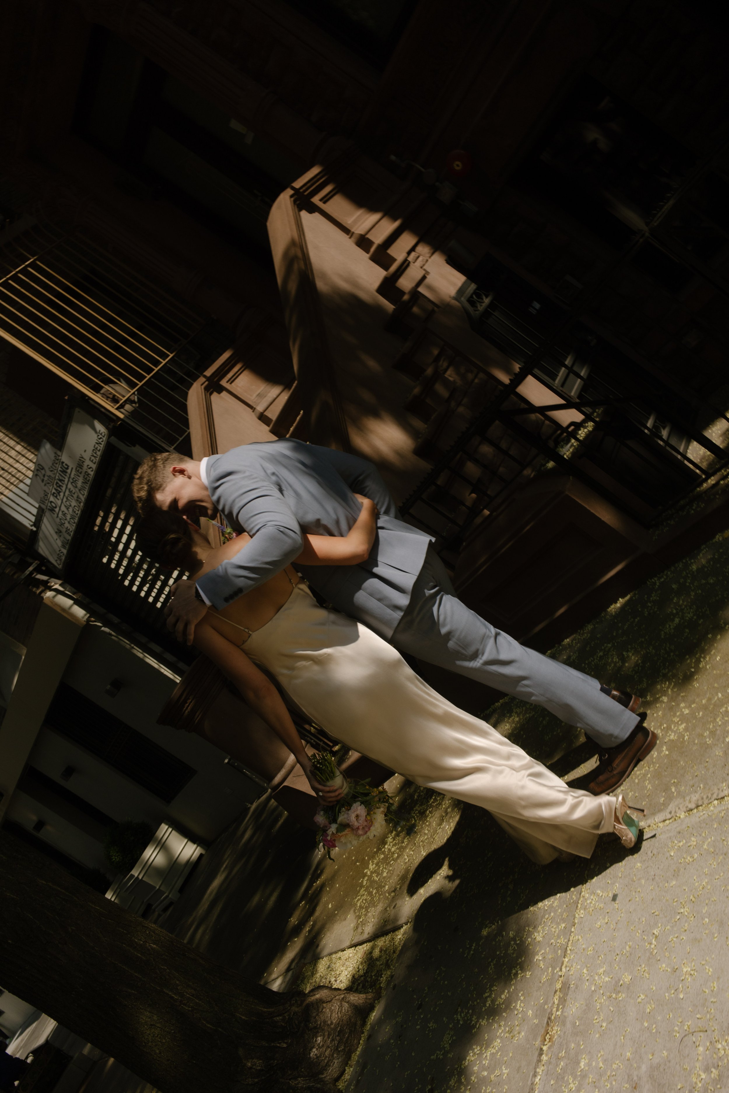 Bride and groom embracing beneath the trees on a city sidewalk near NYC hotels.