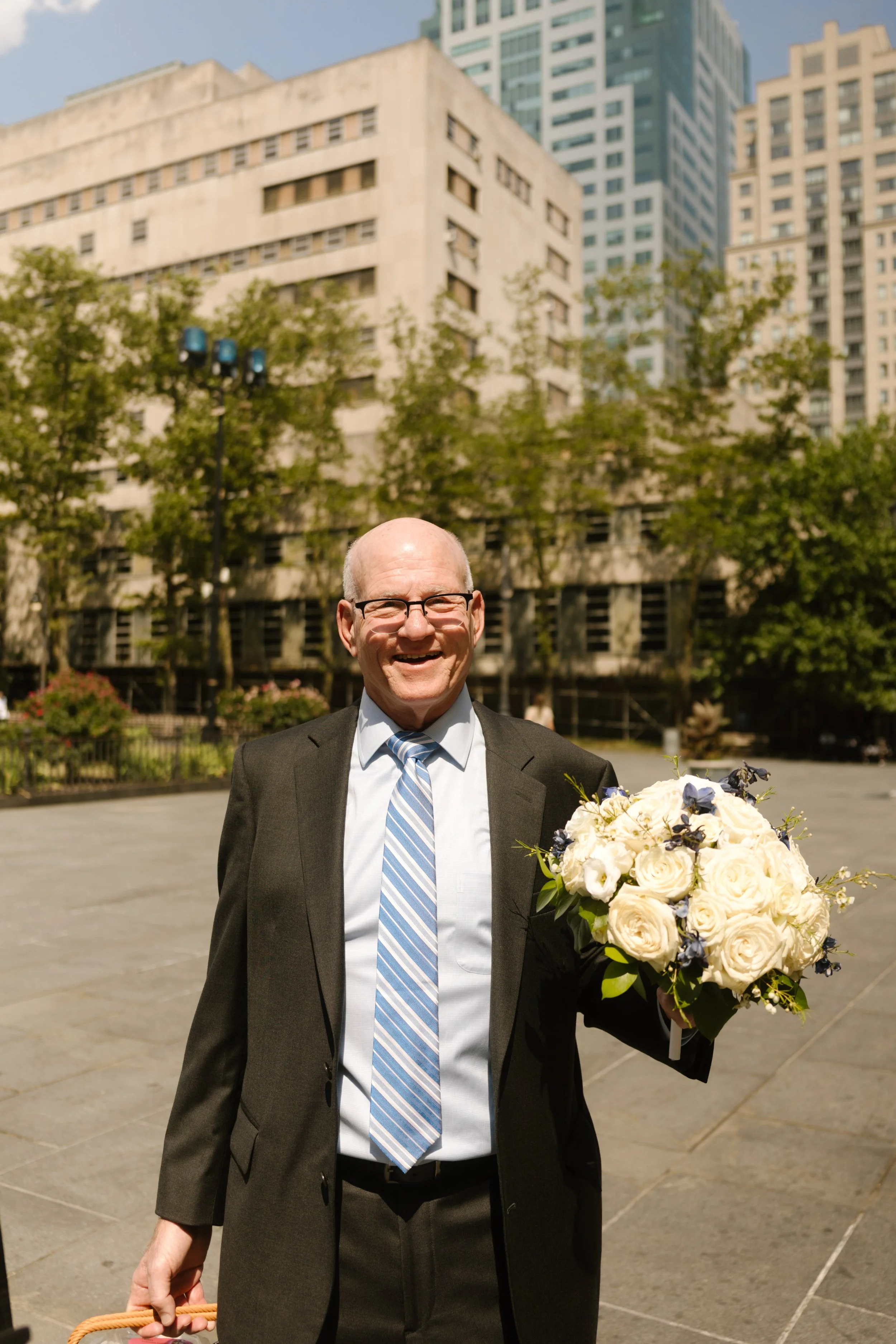Father of the bride holding a bouquet outside City Hall before an intimate New York wedding ceremony.