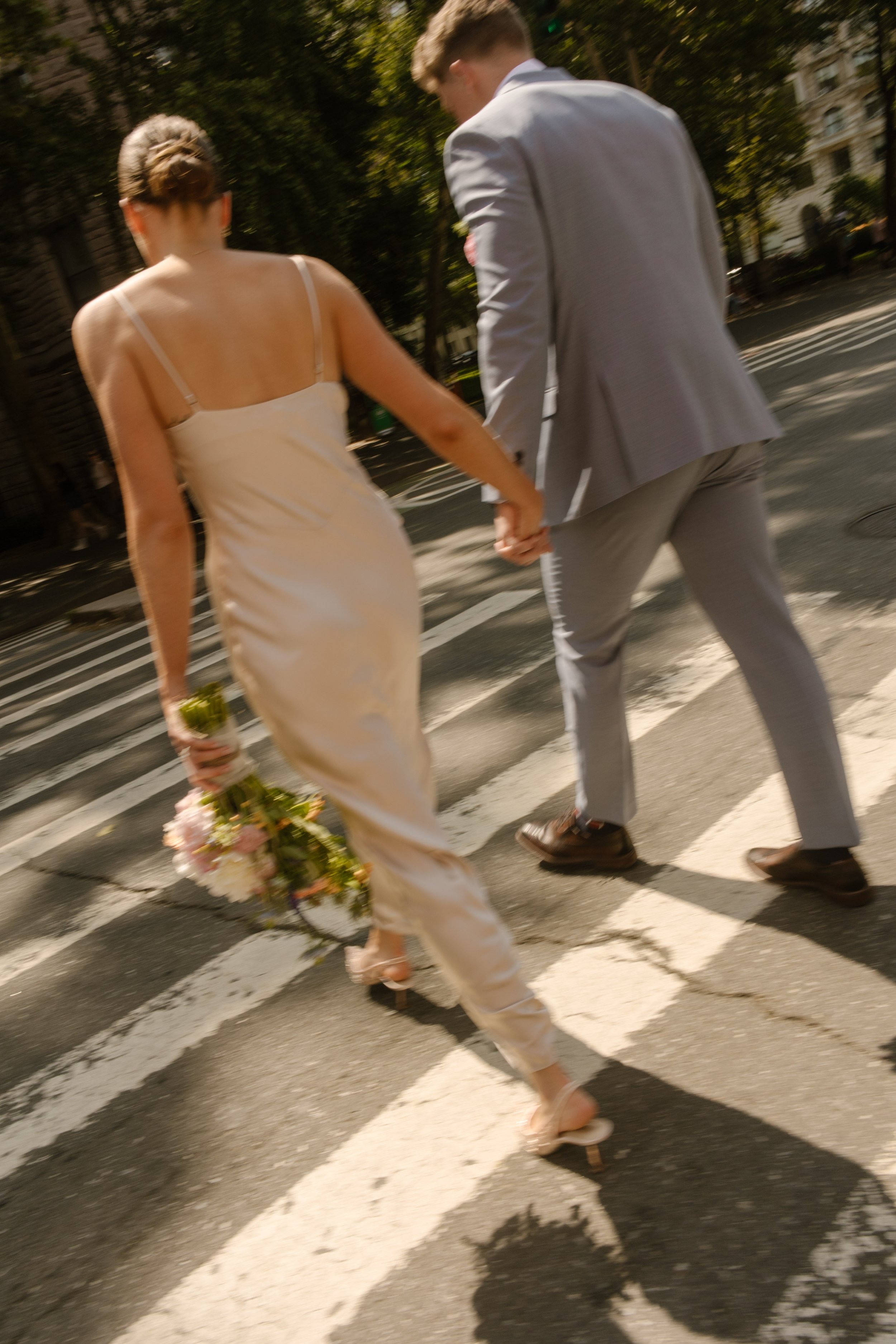 Bride and groom holding hands as they cross a sunny city street near NYC hotels.