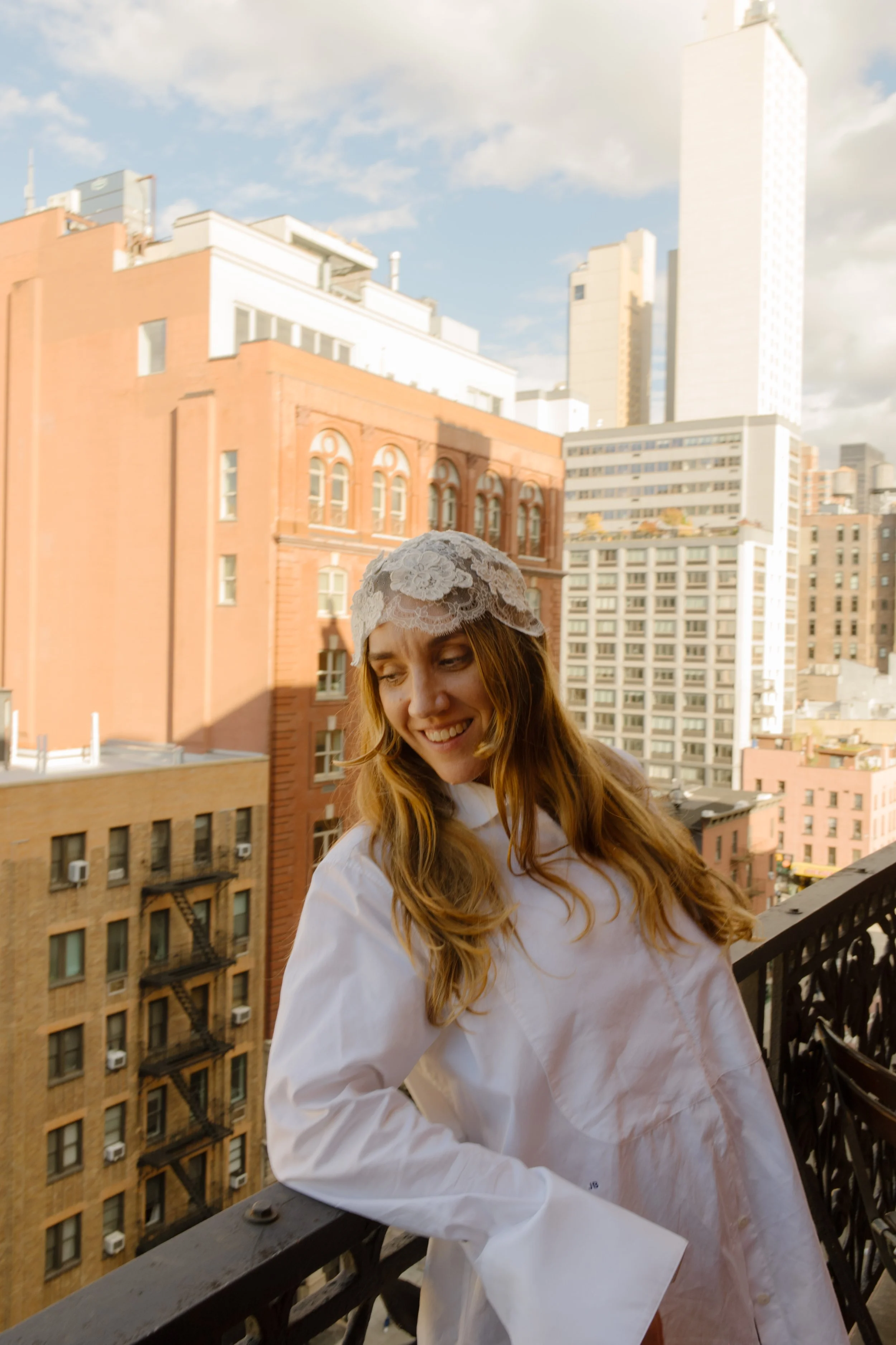 Smiling bride in a white outfit standing on a balcony overlooking New York City near NYC hotels.
