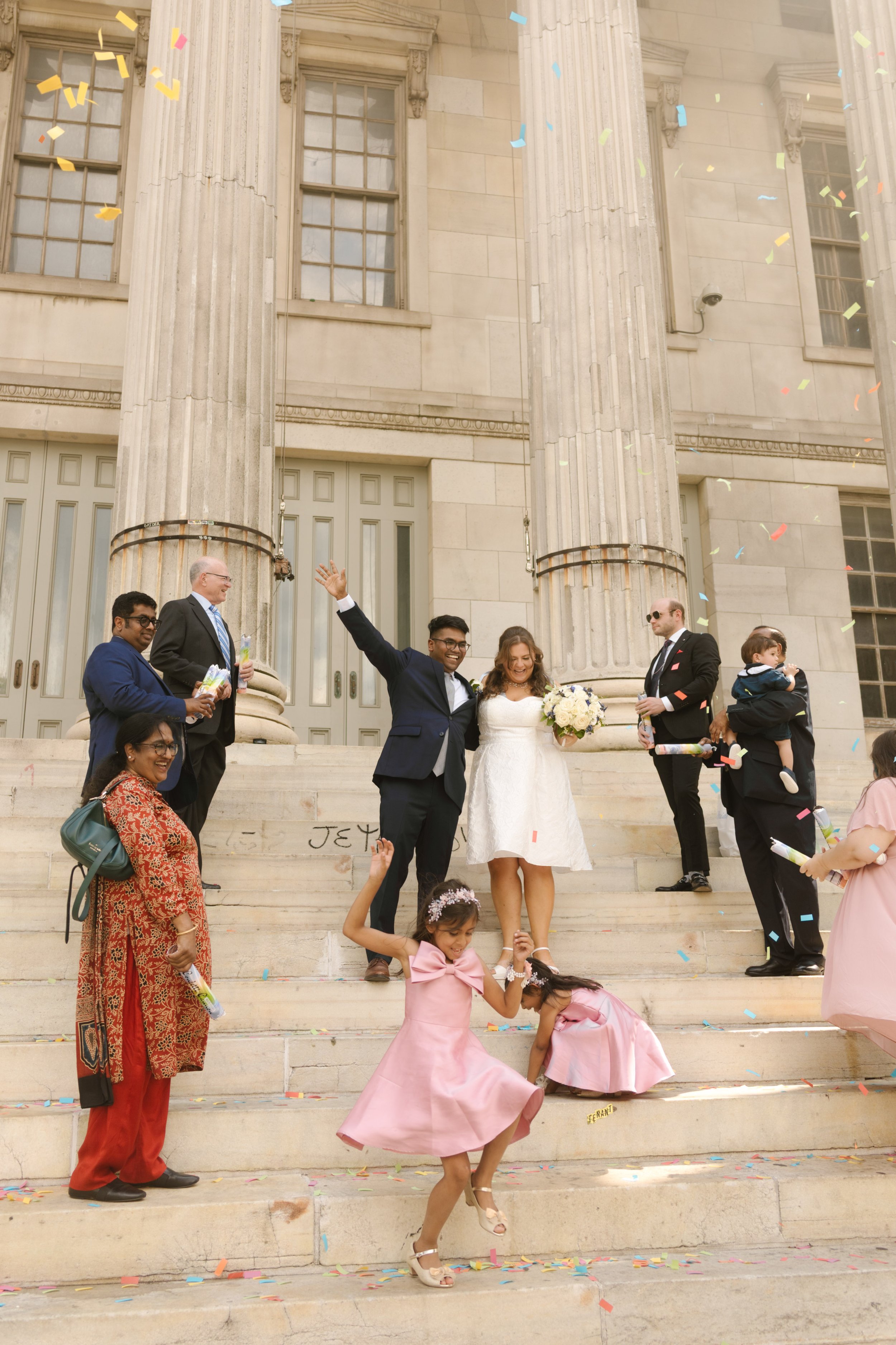 Family celebrates outside New York City Hall with confetti after a courthouse wedding ceremony.