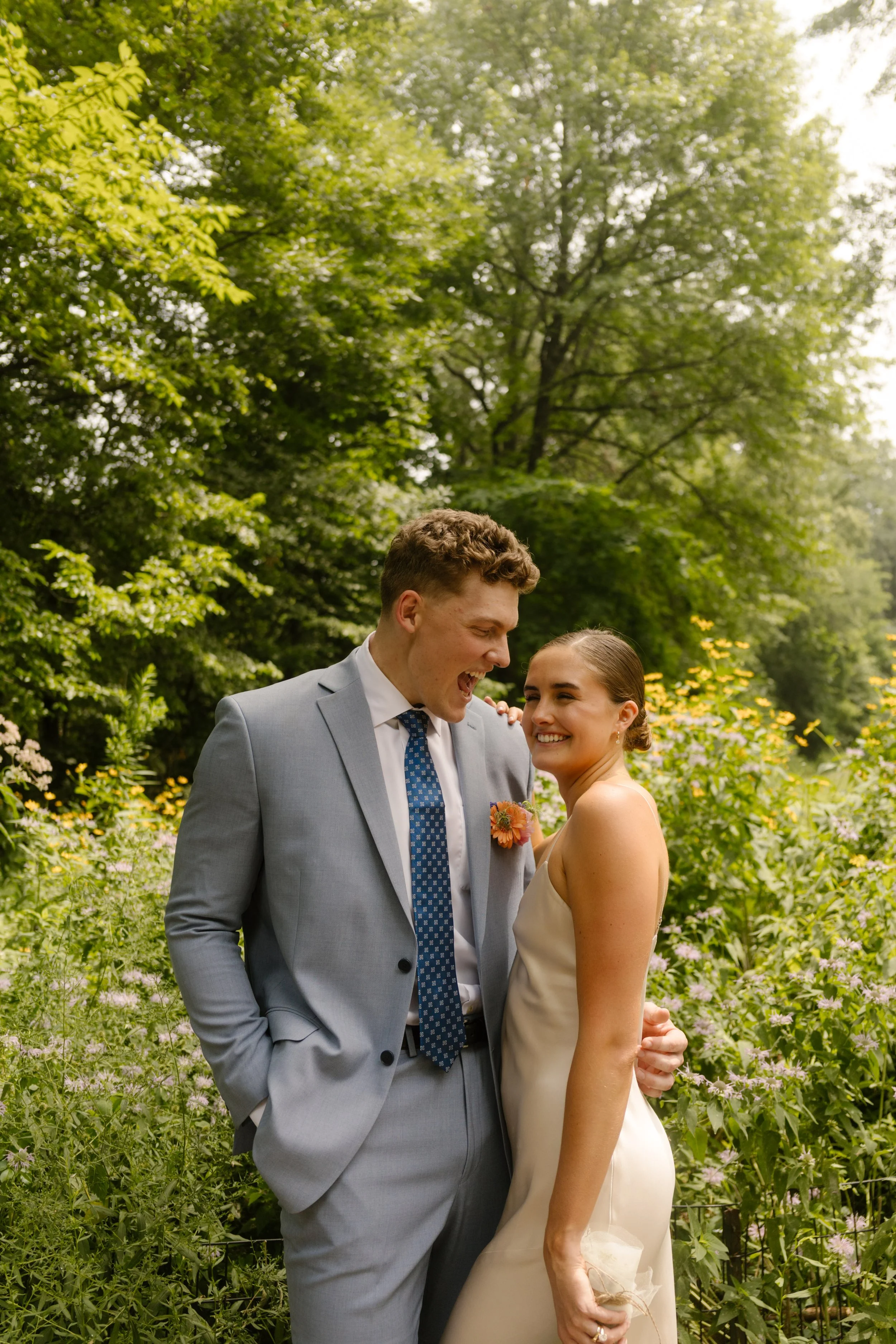 Bride and groom laughing together in a lush garden after leaving one of the nearby NYC hotels for wedding portraits.