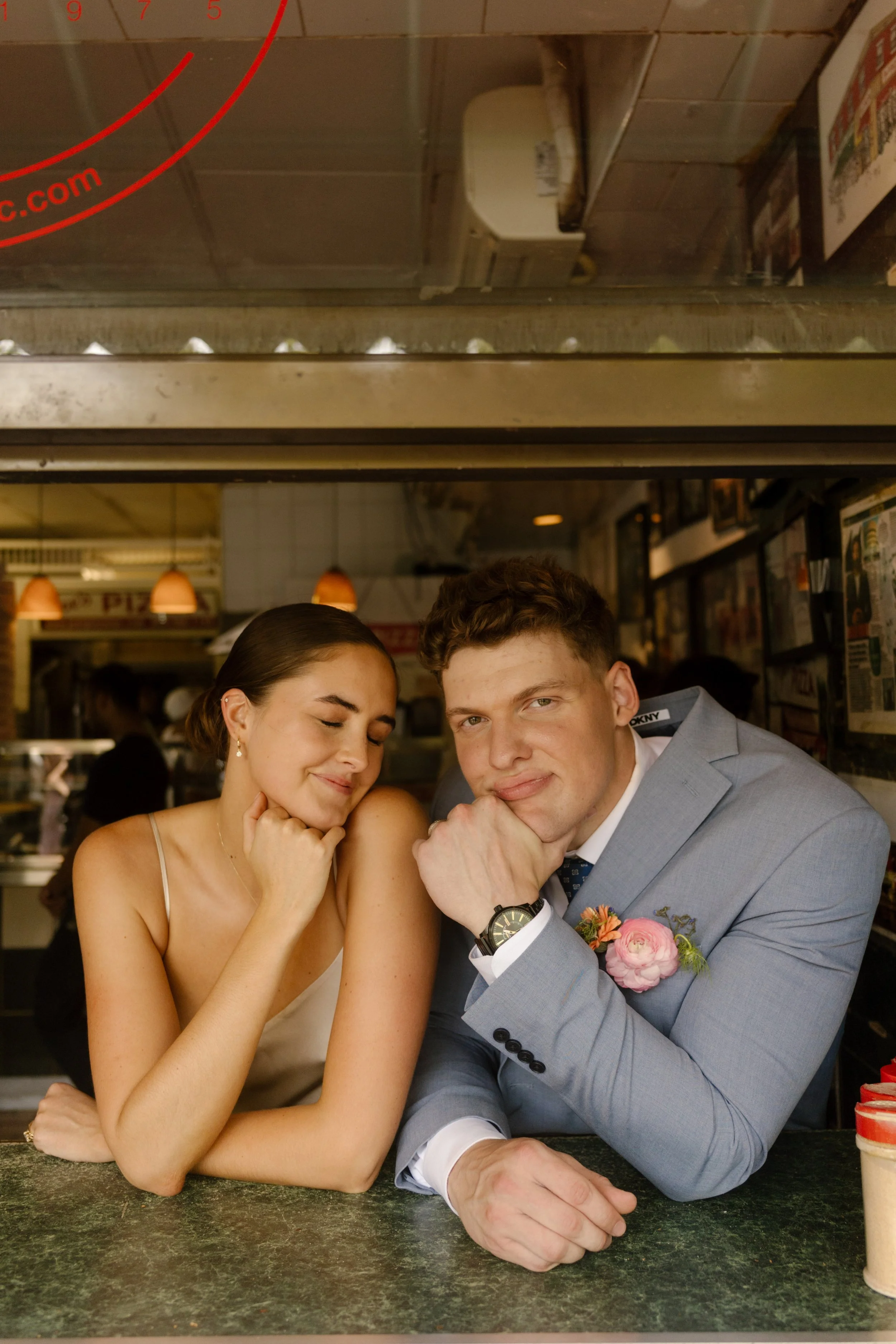 Bride and groom lean out the window of a classic New York diner during their wedding day, capturing playful documentary-style portraits.