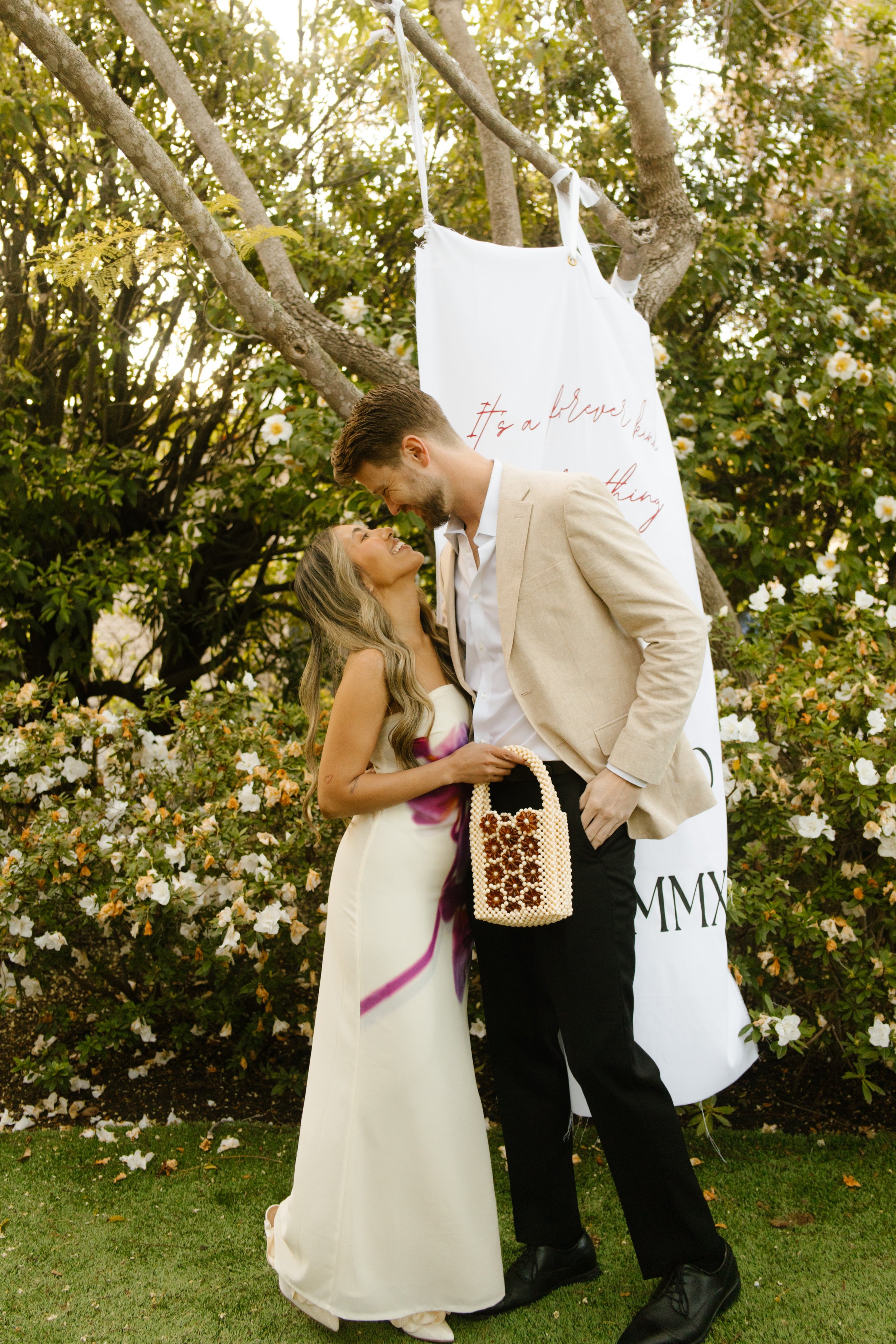 Couple dressed for a welcome party posing together in a garden surrounded by blooming flowers