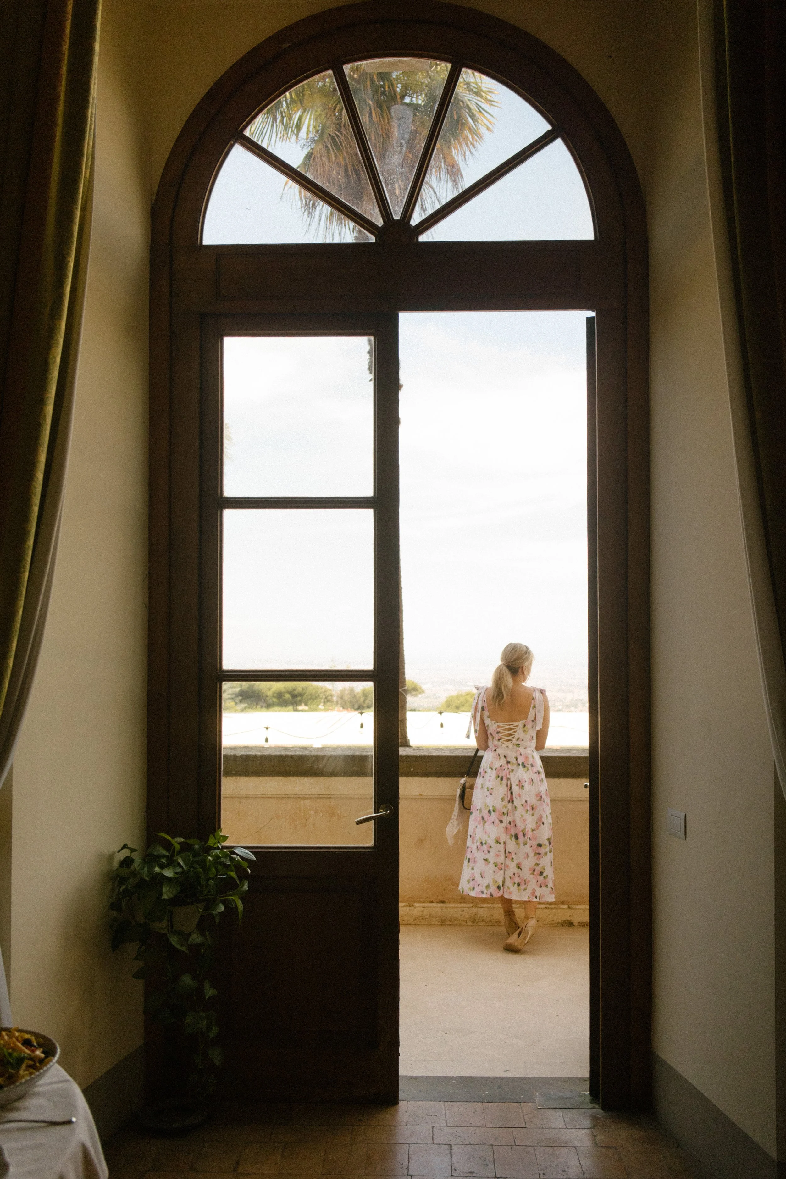 Multi-Day Destination Wedding guest in a floral dress standing on a balcony framed by a tall arched doorway