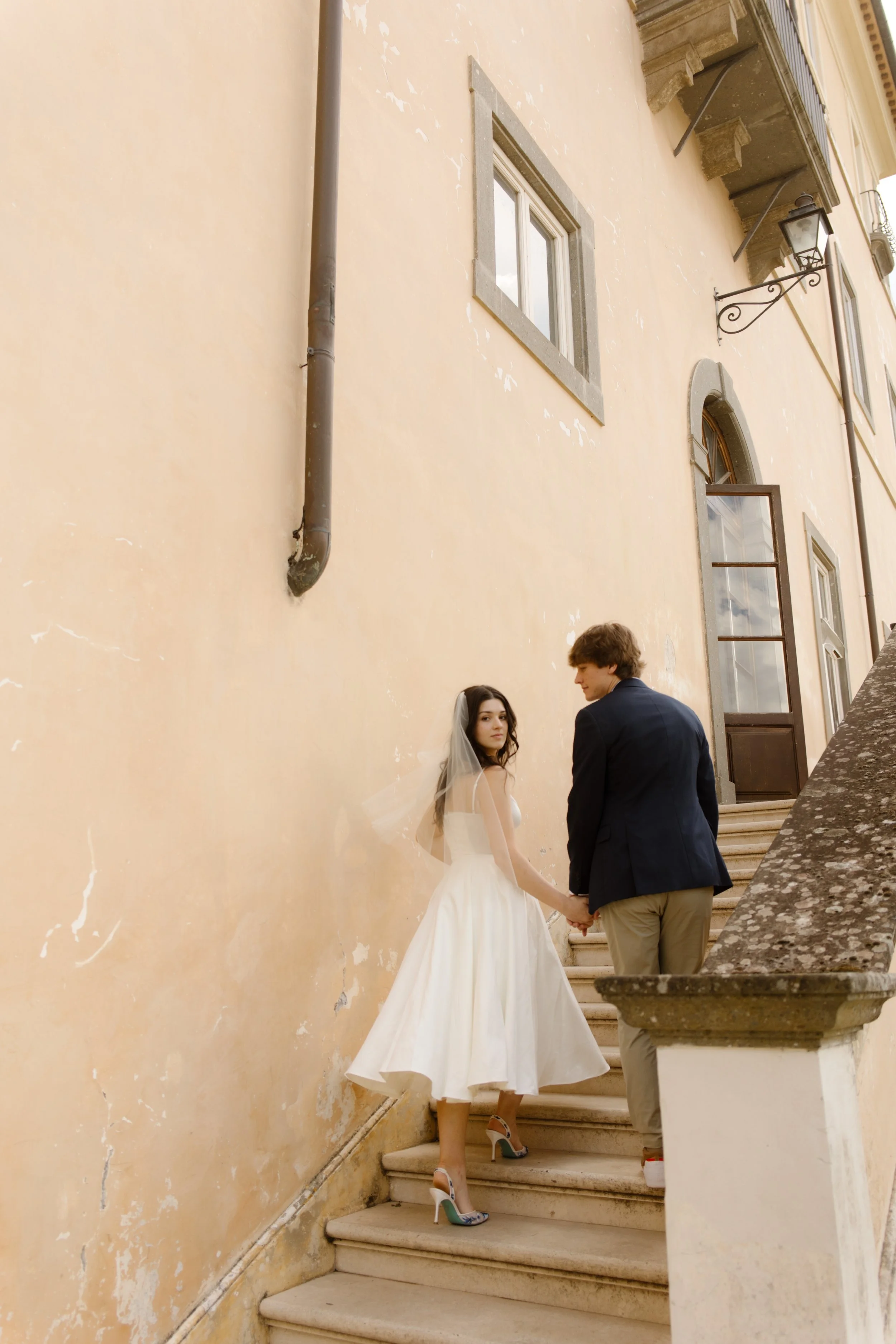 Newlywed couple holding hands while walking up the steps of a historic Italian villa