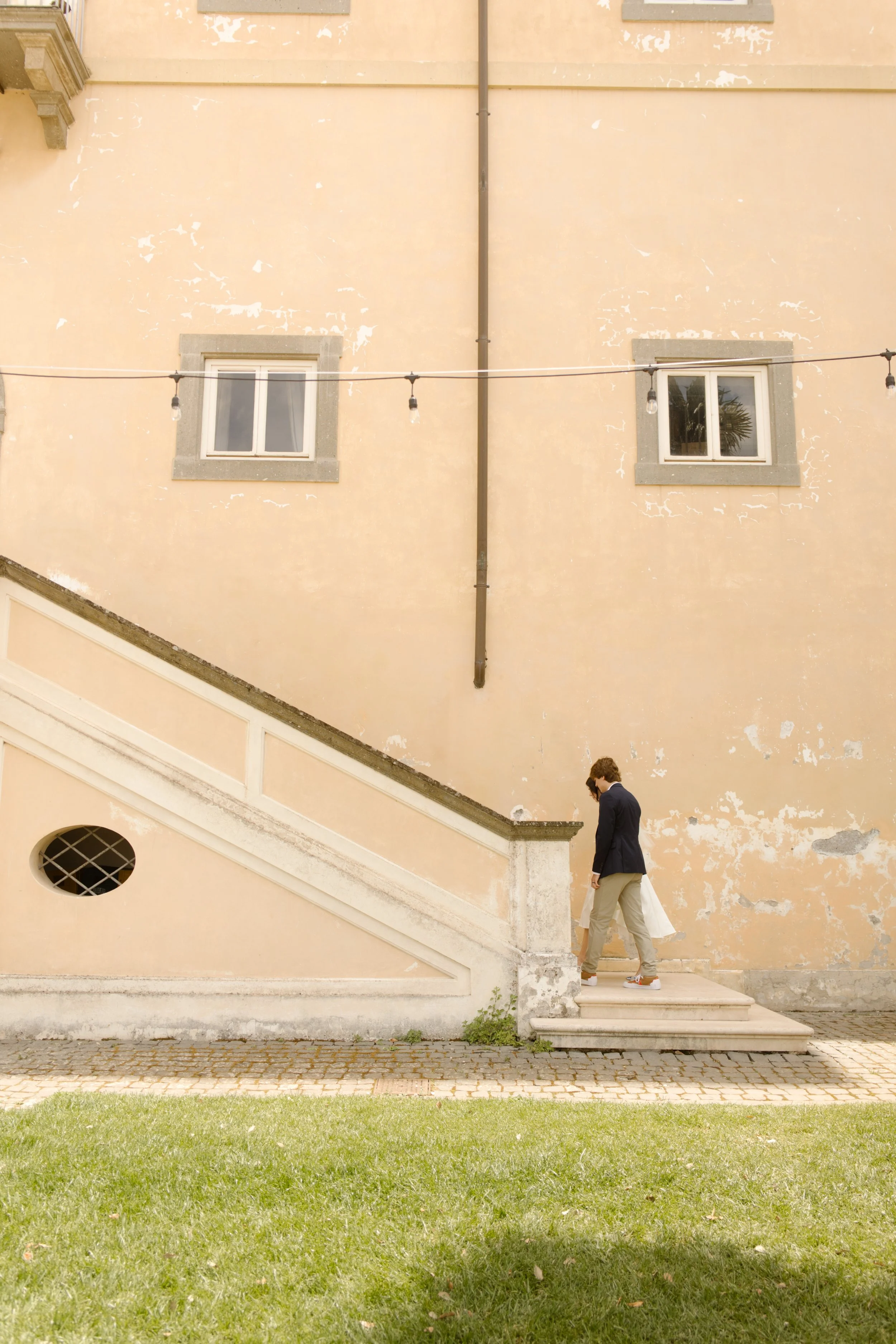 Newlywed couple walking hand in hand along the steps of a historic villa during their destination wedding weekend