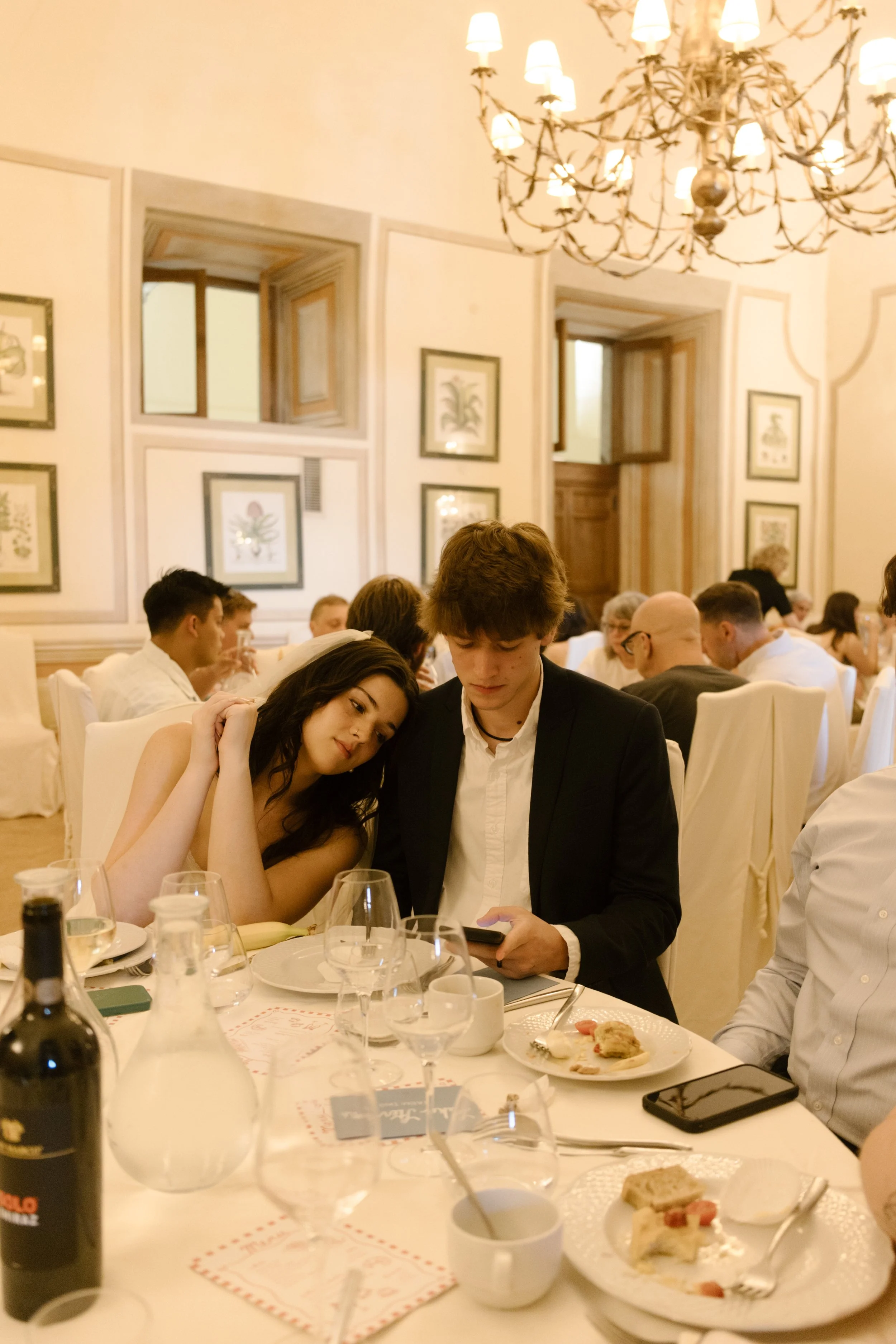 Newlywed couple sitting together at dinner surrounded by friends and family during their destination wedding reception