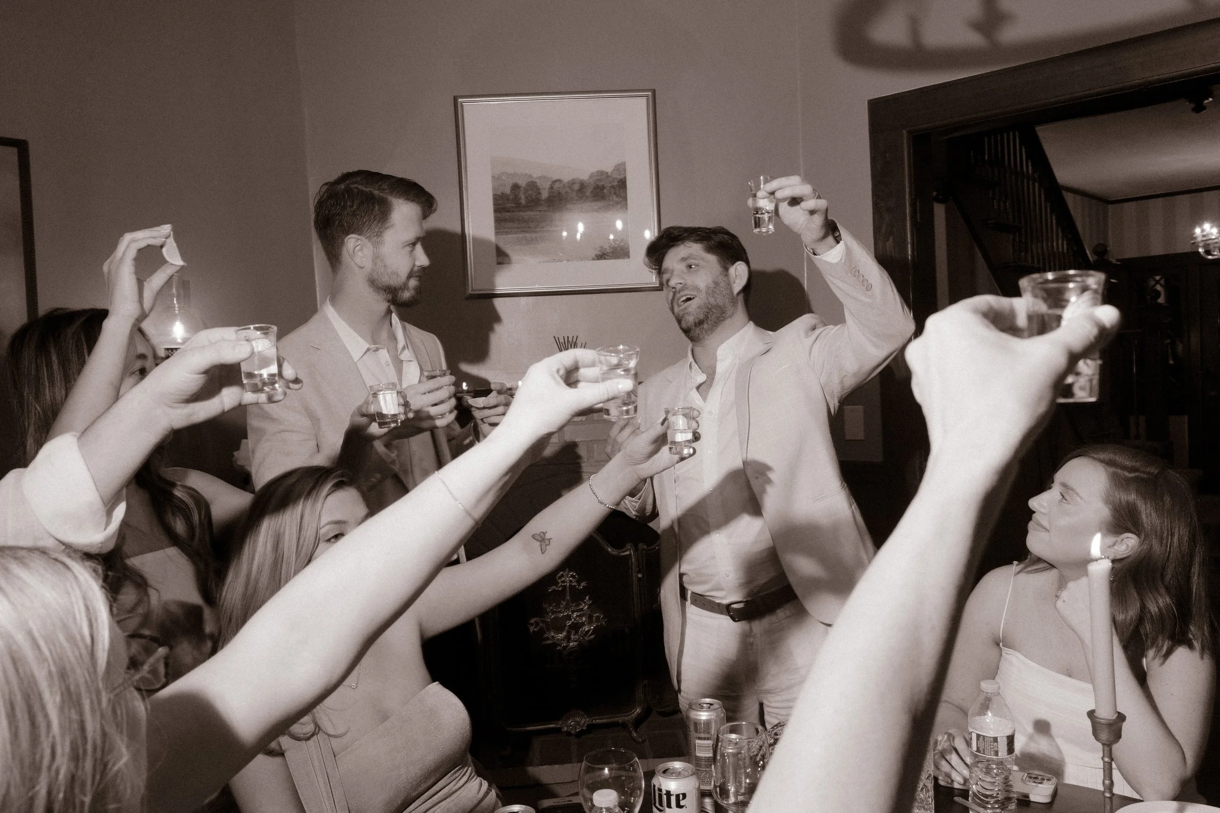 Wedding guests raising shot glasses together during a candid black-and-white wedding weekend celebration