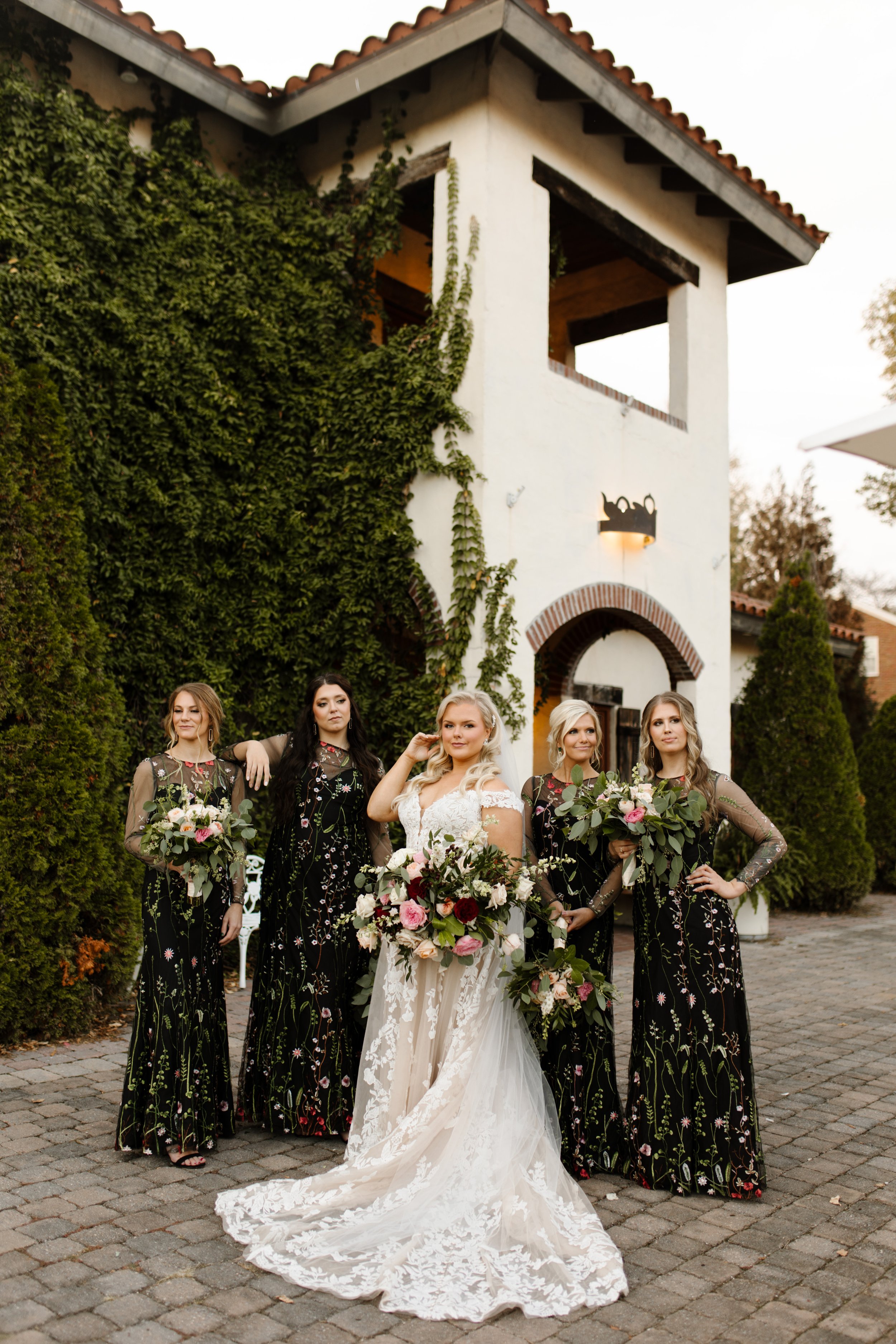 Bride posing with her bridesmaids in floral dresses outside an ivy-covered wedding venue