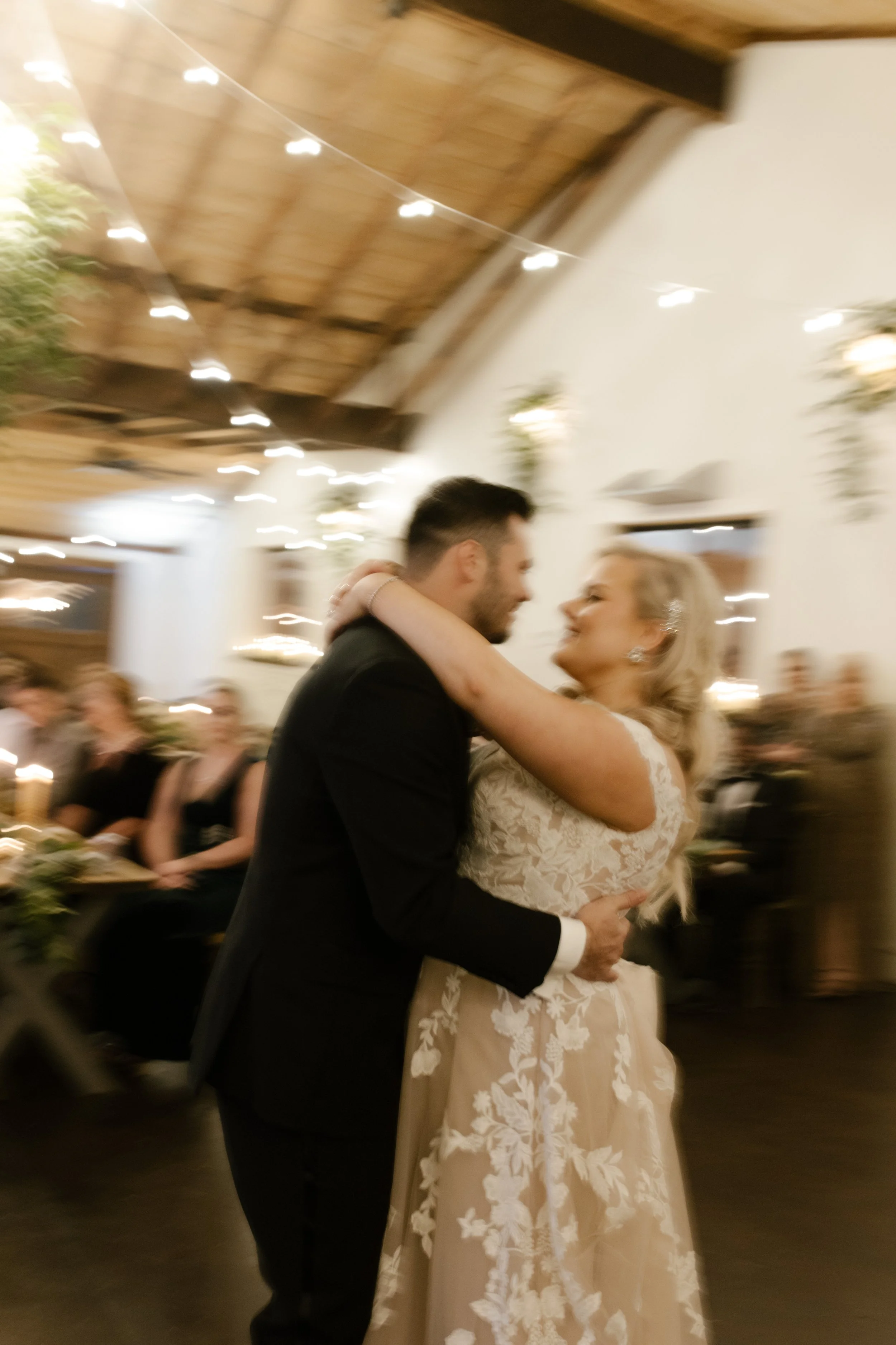 Bride and groom dancing together beneath string lights during their lively wedding reception