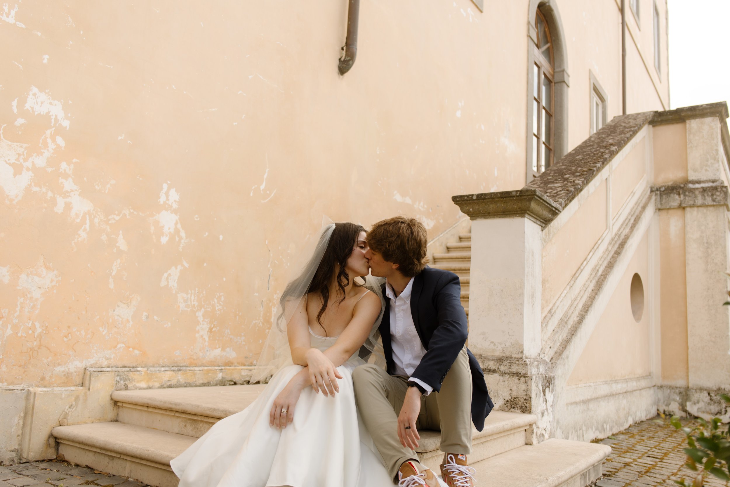 Newlywed couple kissing on the steps of a historic Italian villa during their destination wedding