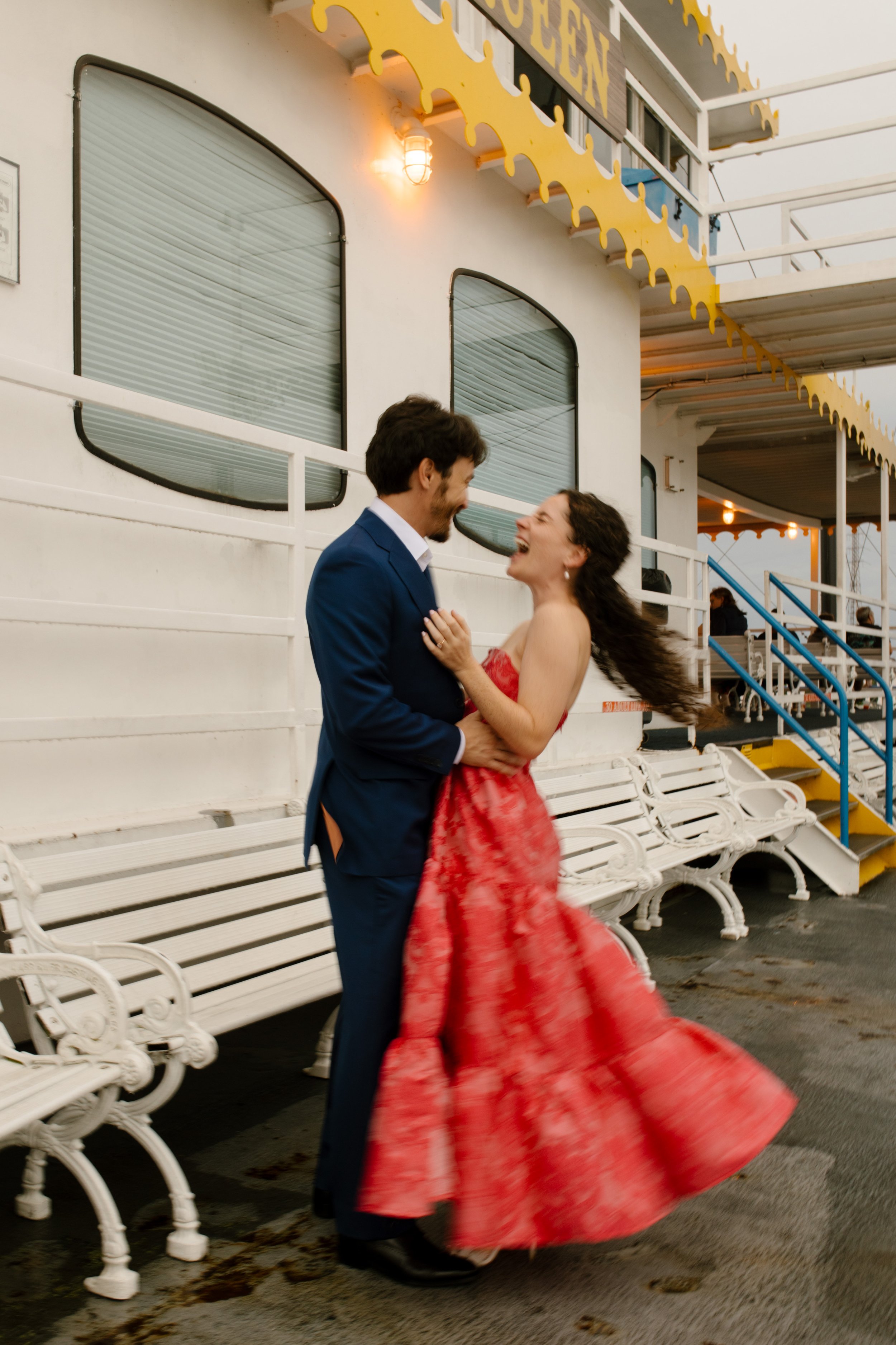 Couple laughing and dancing together on a boat during their wedding rehearsal dinner celebration.